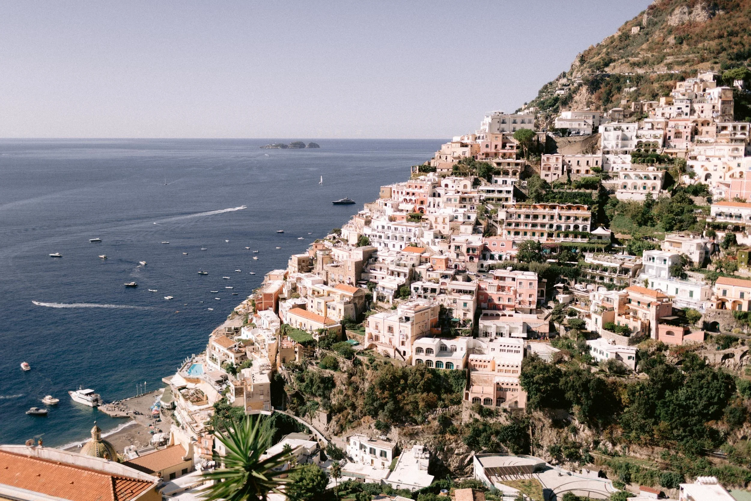 Cliffside view of a coastal town with pastel-colored buildings and boats in the water.