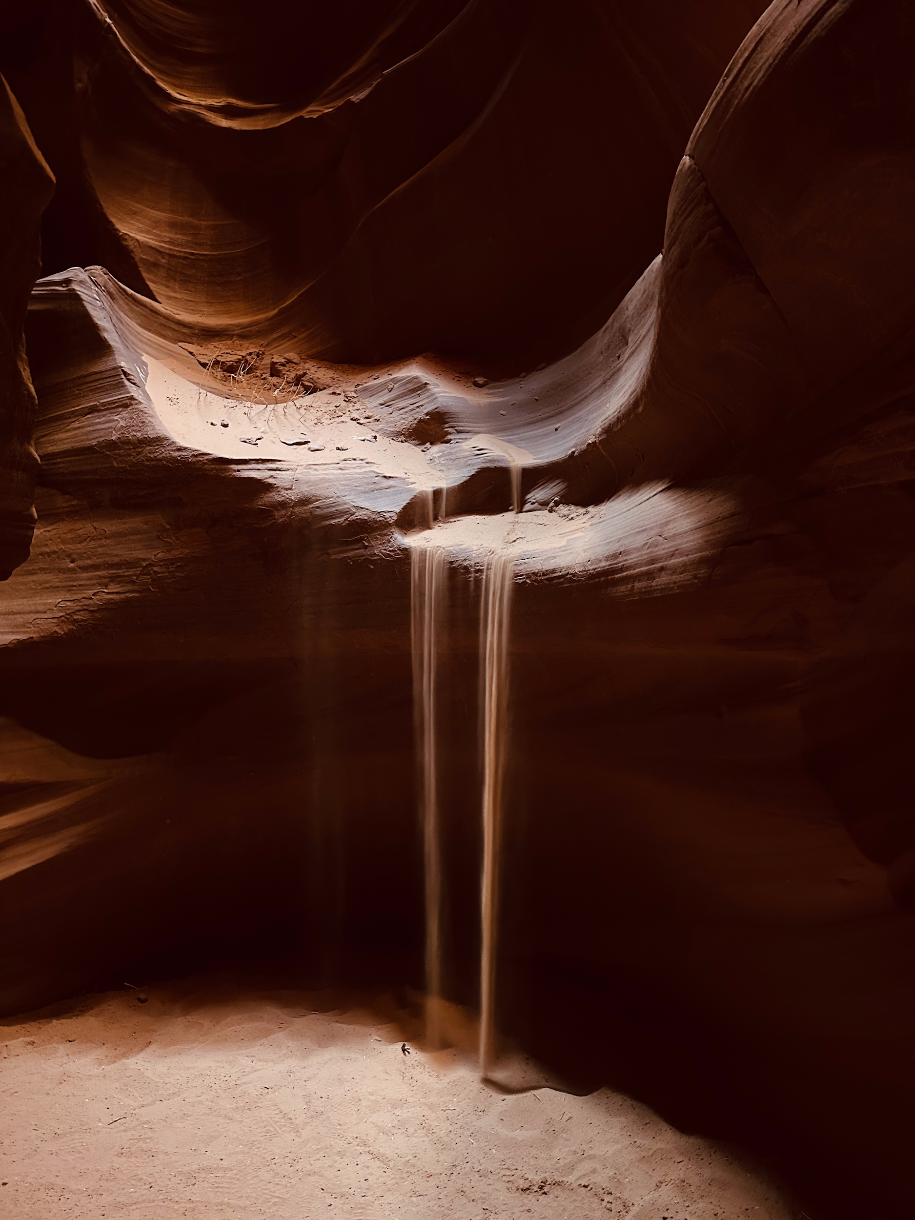 Two thin streams of sand falling from the top of a dark Southwest canyon.