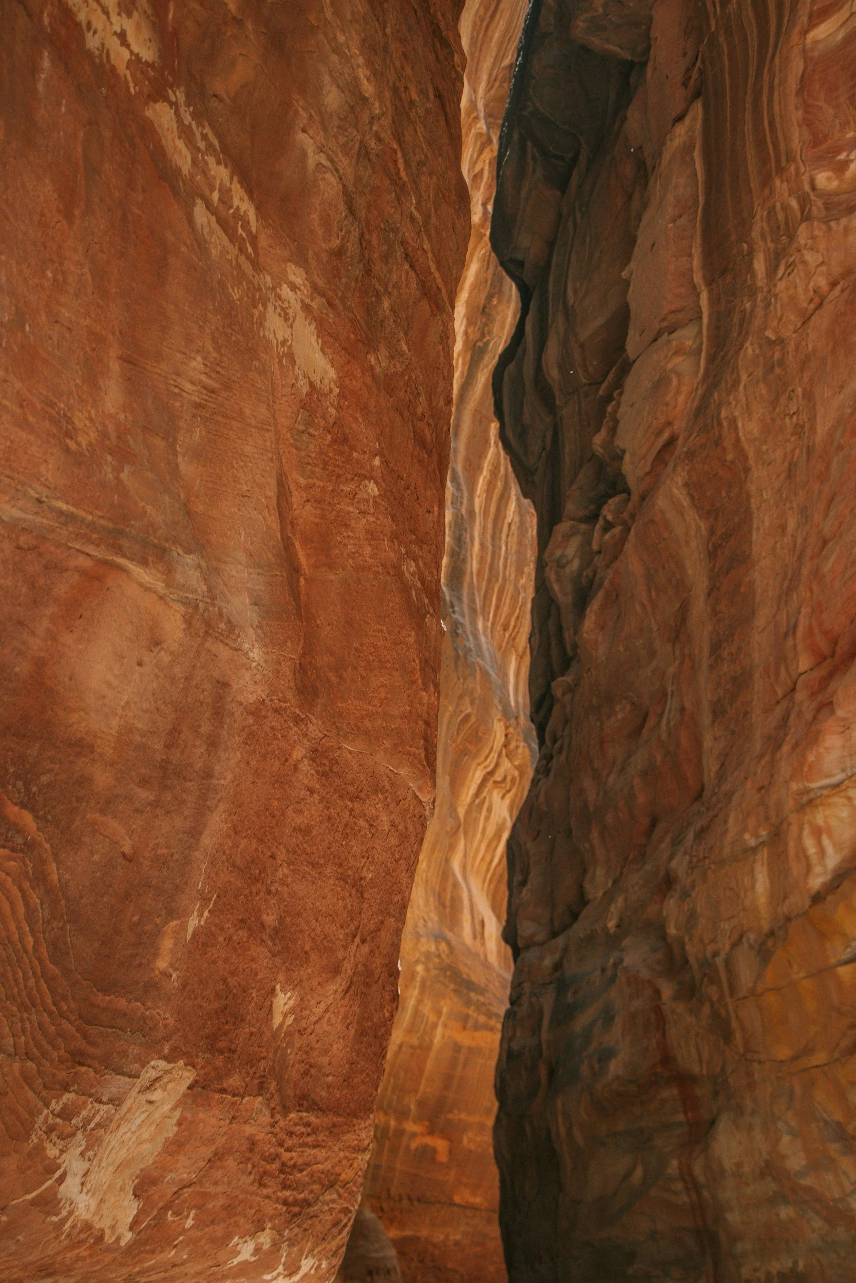 Narrow slot canyon in the Southwest with smooth, layered sandstone walls in shades of red, orange, and brown.