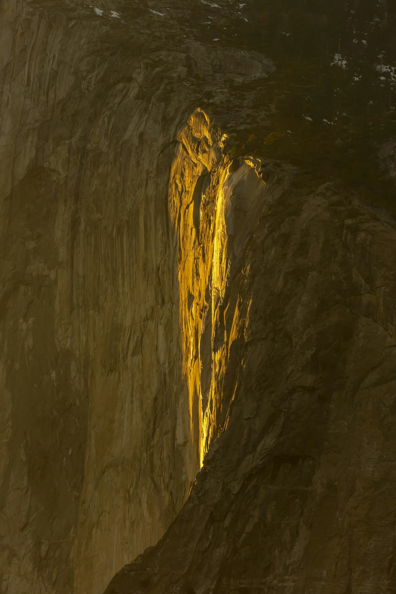 Sunlit waterfall cascading over a large cliff.