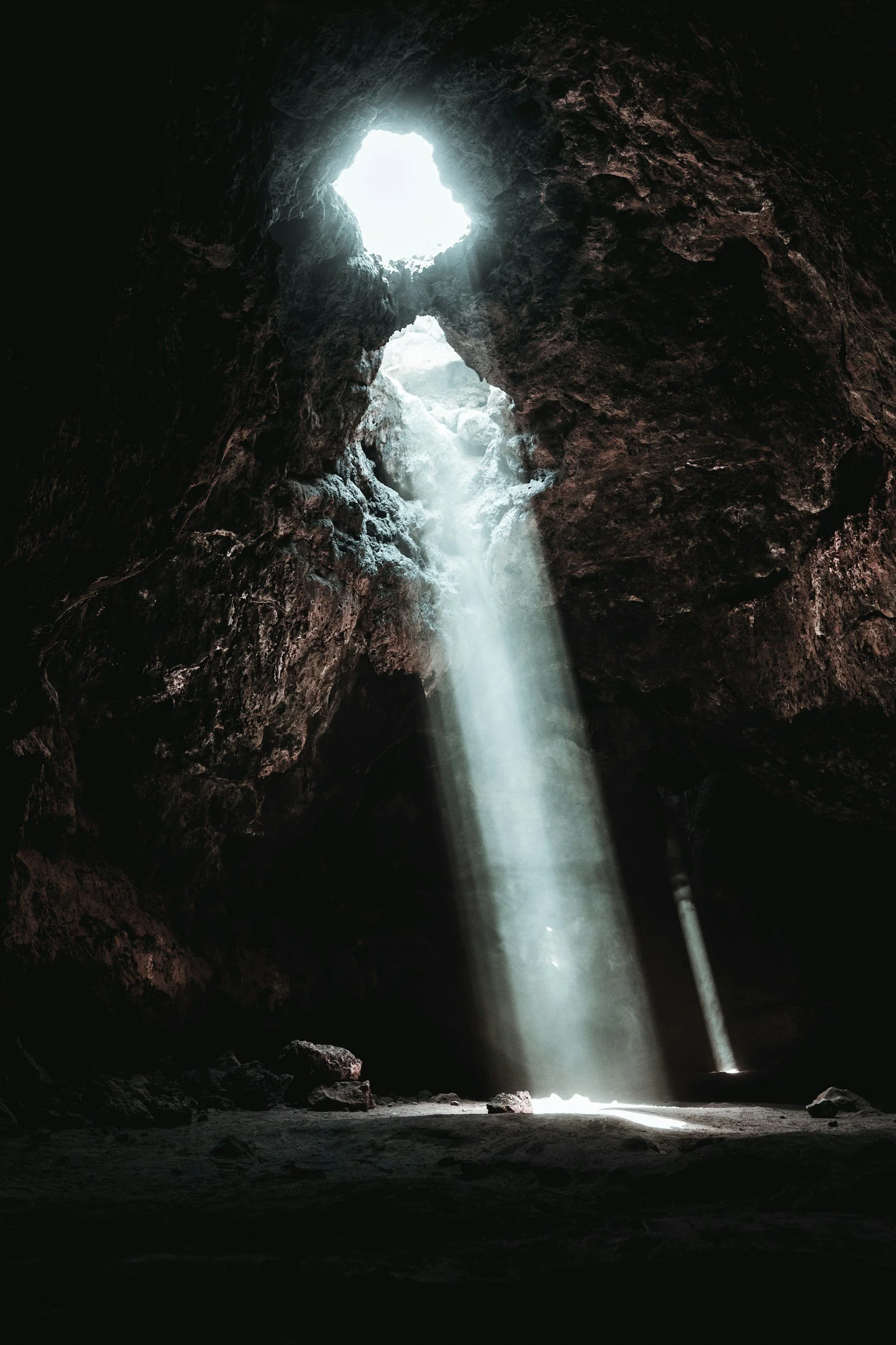 A dark cave with sunlight coming through an opening at the top and casting a ray of light on the cave floor.