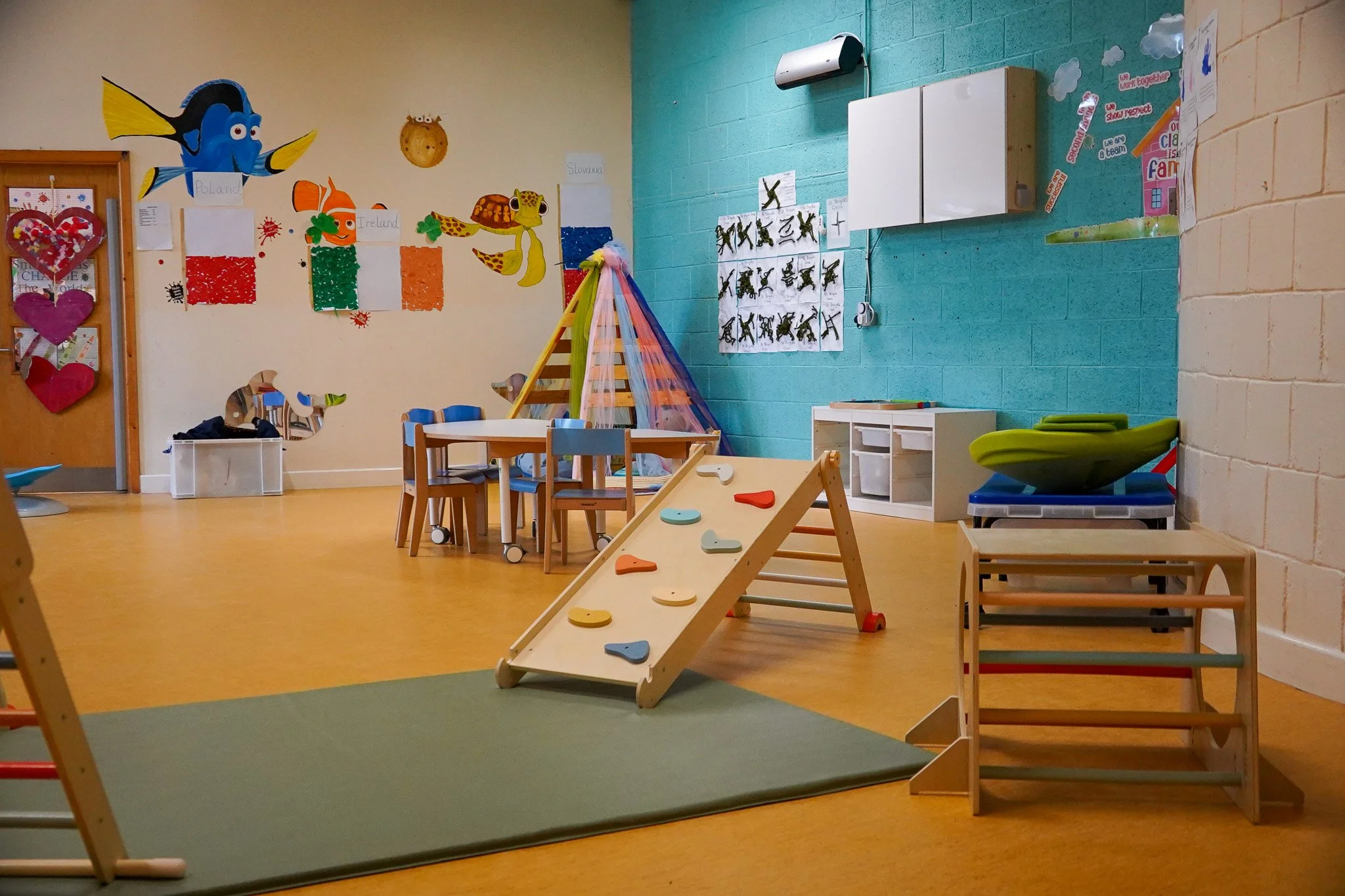 Children's playroom with a climbing ramp, small table and chairs, colorful wall decorations, and educational posters.