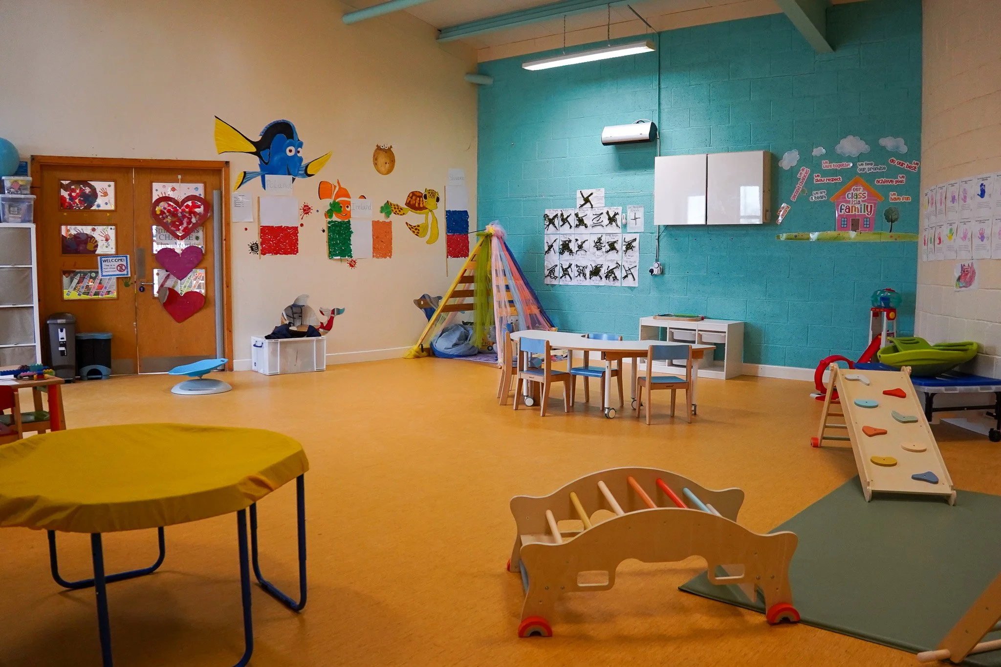 Interior of a preschool classroom with colorful decorations, children's furniture, play area, and educational materials.
