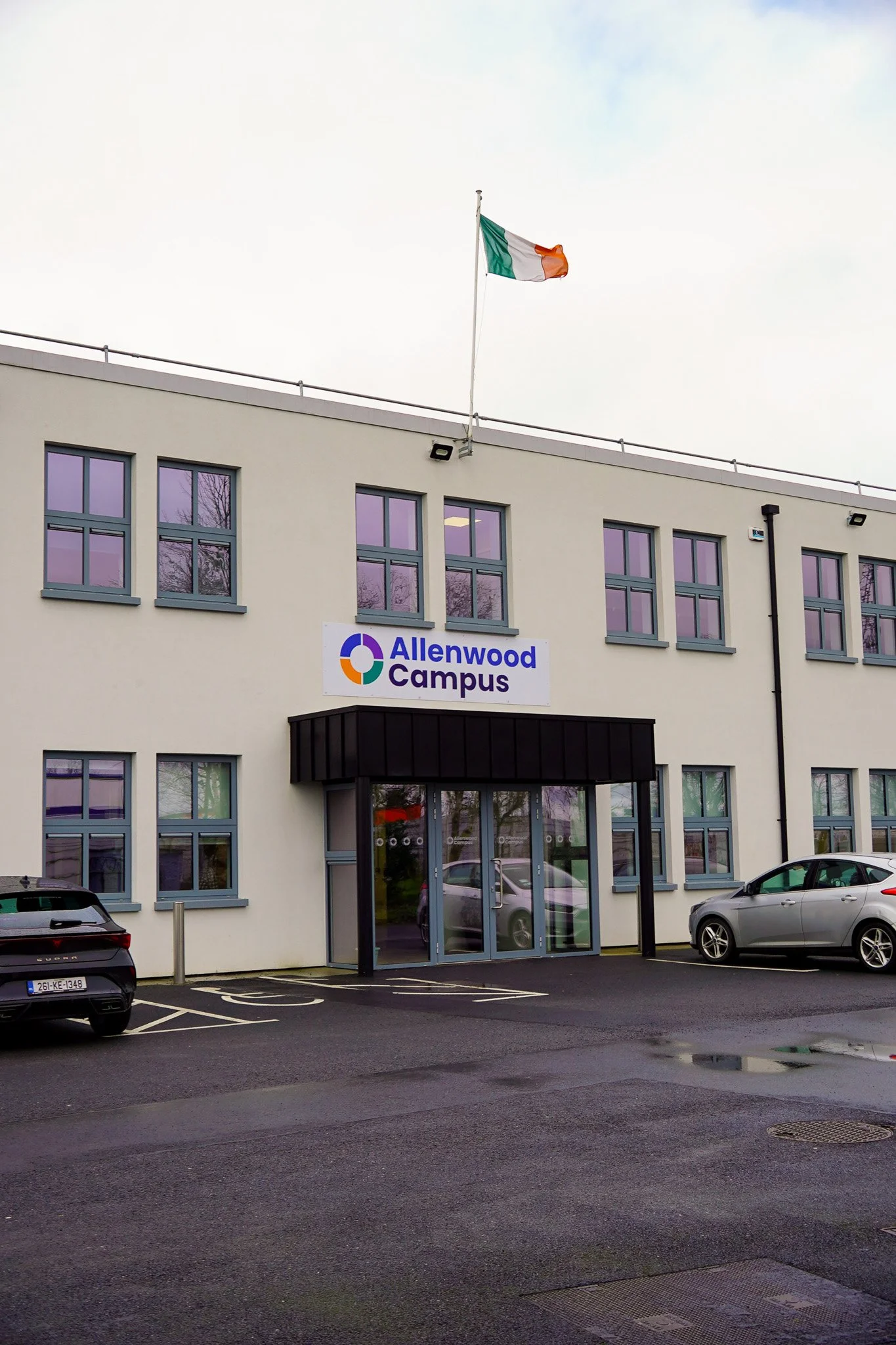 Photo of the Allenwood Campus building with a parked car in front and an Irish flag on top.
