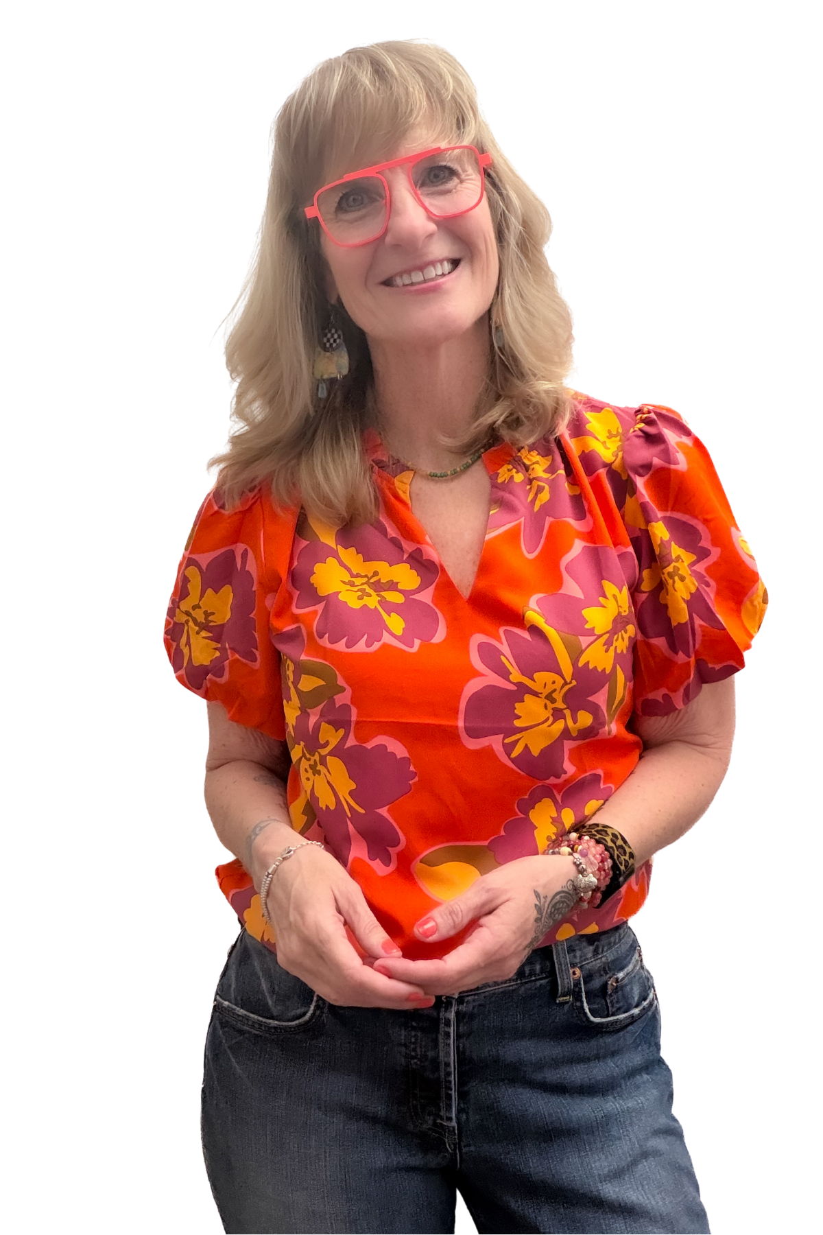 Pamela standing in denim jeans, red, pink, orange short-sleeved shirt, smiling with orange aviator style glasses