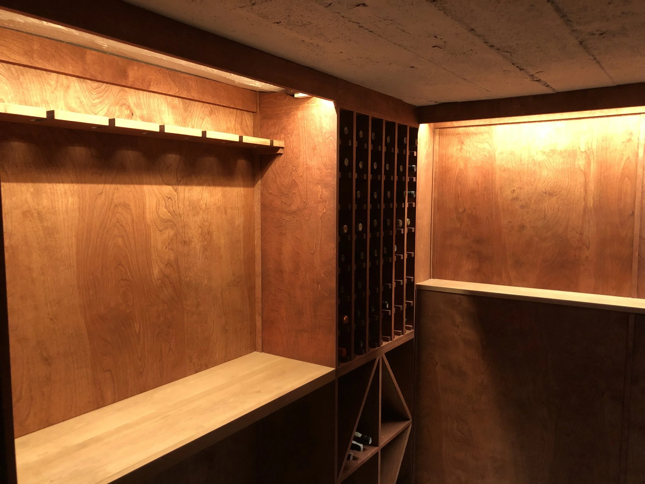 View inside a small wooden wine cellar with shelving for wine bottles and storage, made of natural wood panels.