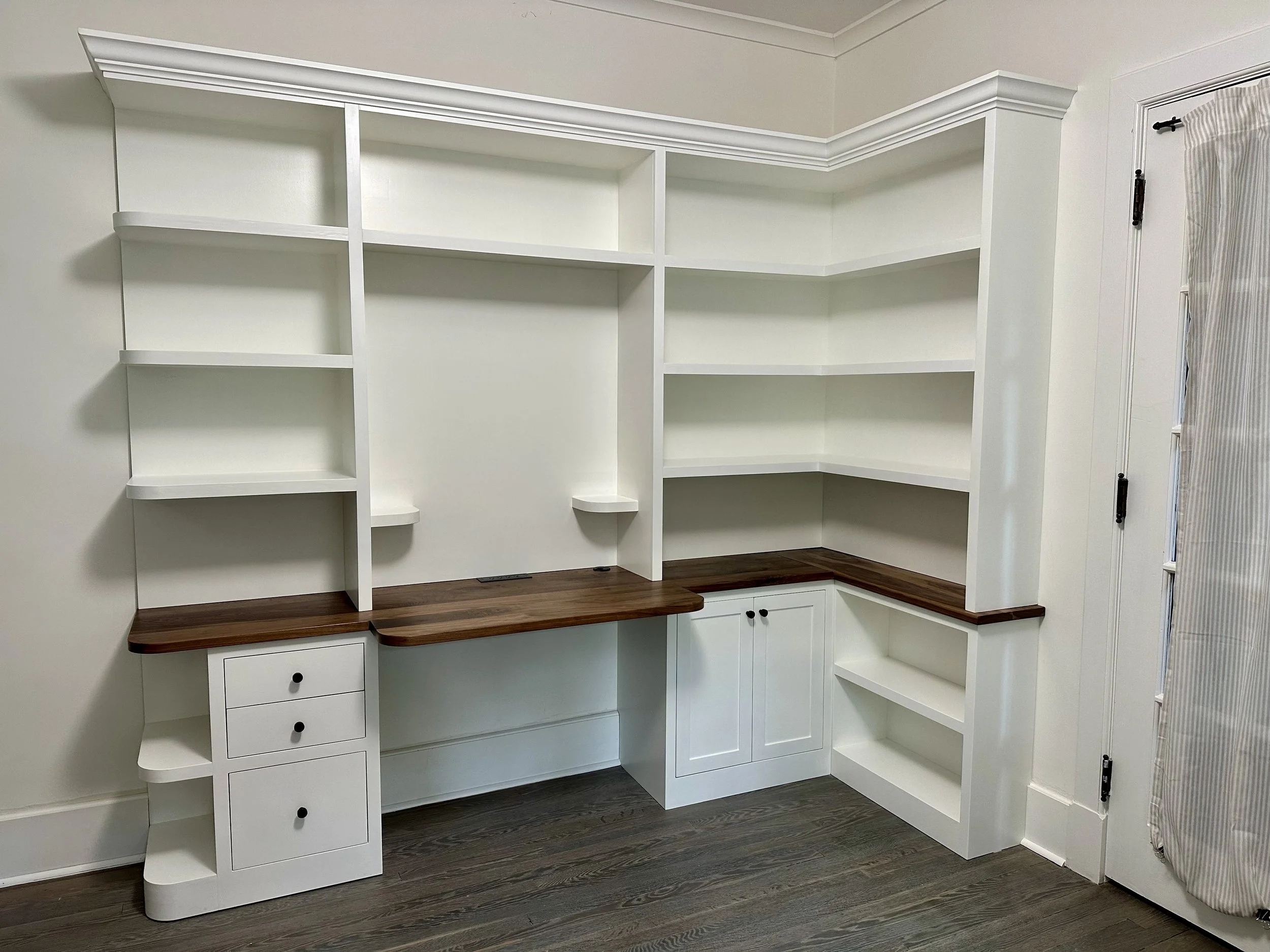Empty white built-in bookshelf with dark wood countertop and small storage drawers and cabinets.