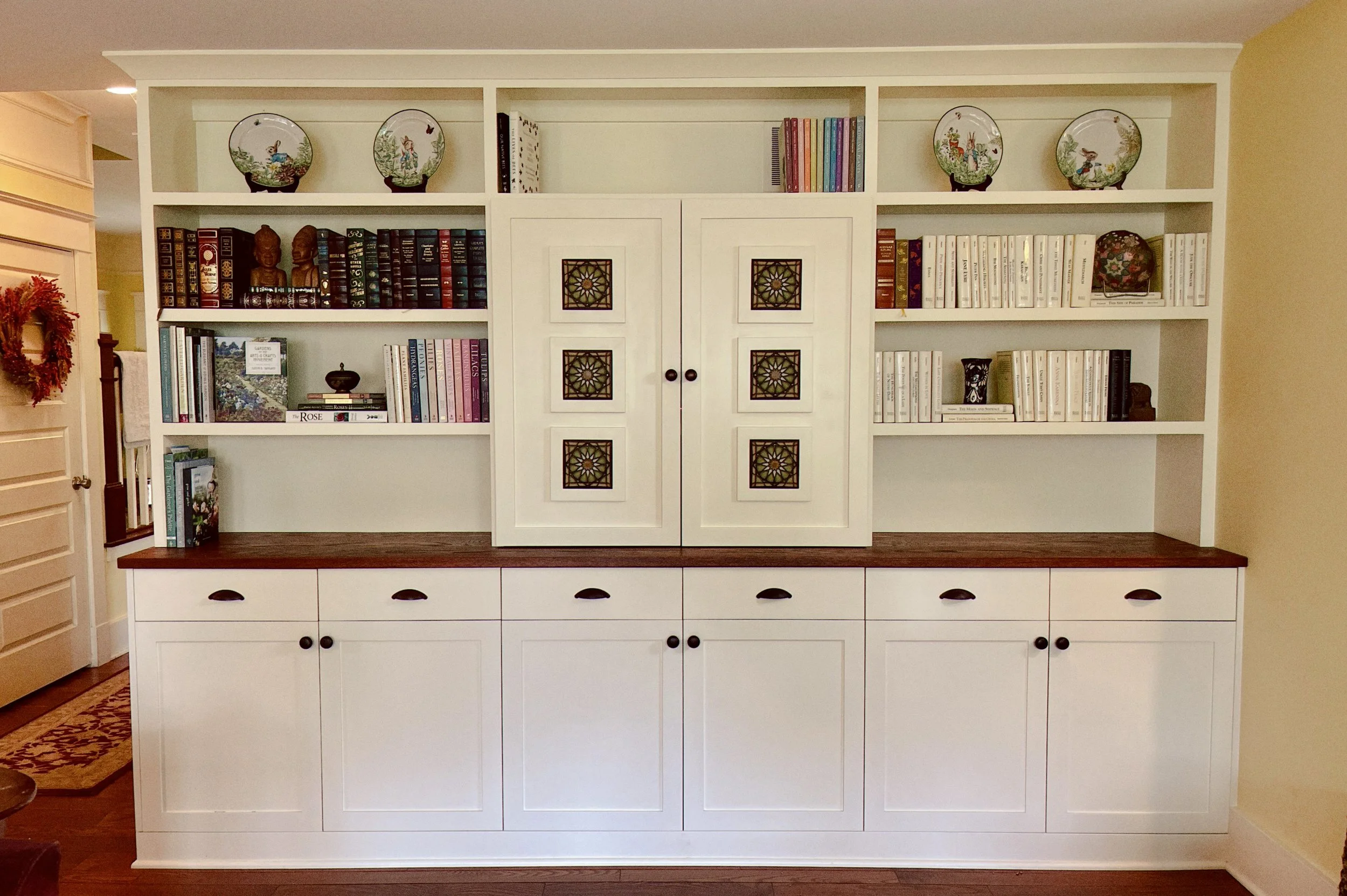 White built-in bookshelf with decorative items and books, along with cabinet doors and drawers, in a living room.
