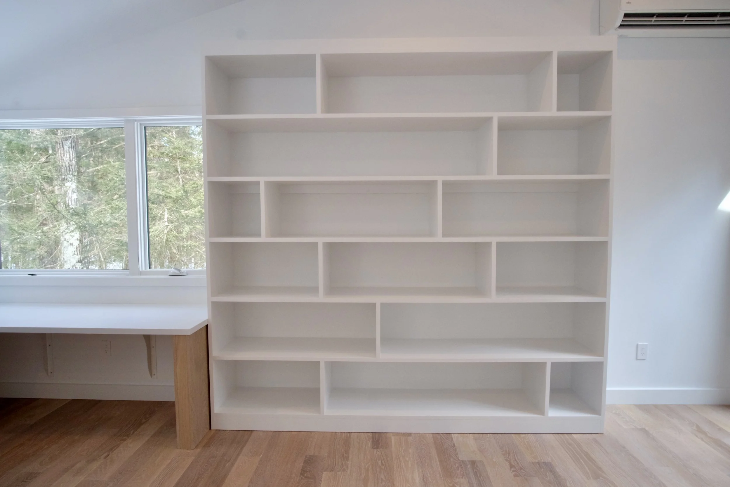 Empty white bookshelf in a room with a window showing trees outside.