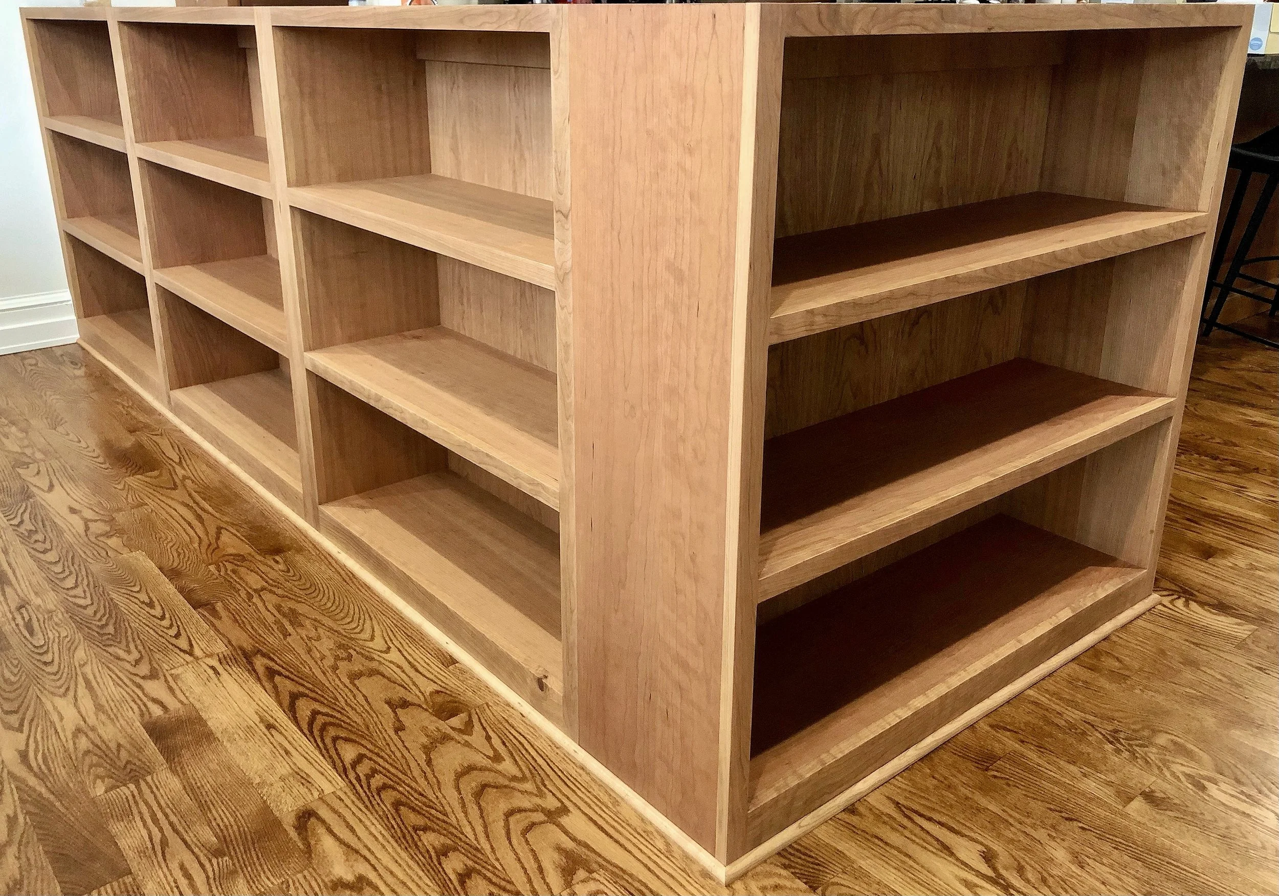Unfinished wooden bookshelf with multiple open shelves, placed on a hardwood floor.
