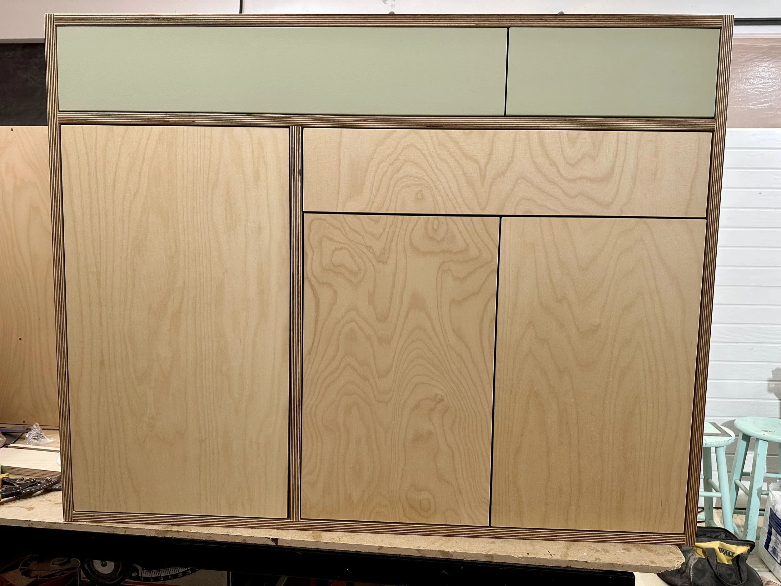 unfinished wooden cabinet with multiple compartments and drawers in a workshop setting.