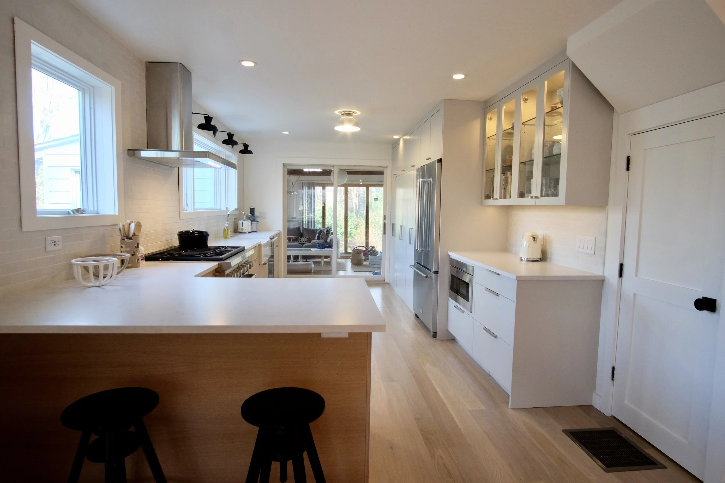 Bright, modern kitchen with white cabinets, wood accents, and stainless steel appliances, including a refrigerator and microwave, overlooking a sunroom with sliding glass doors.