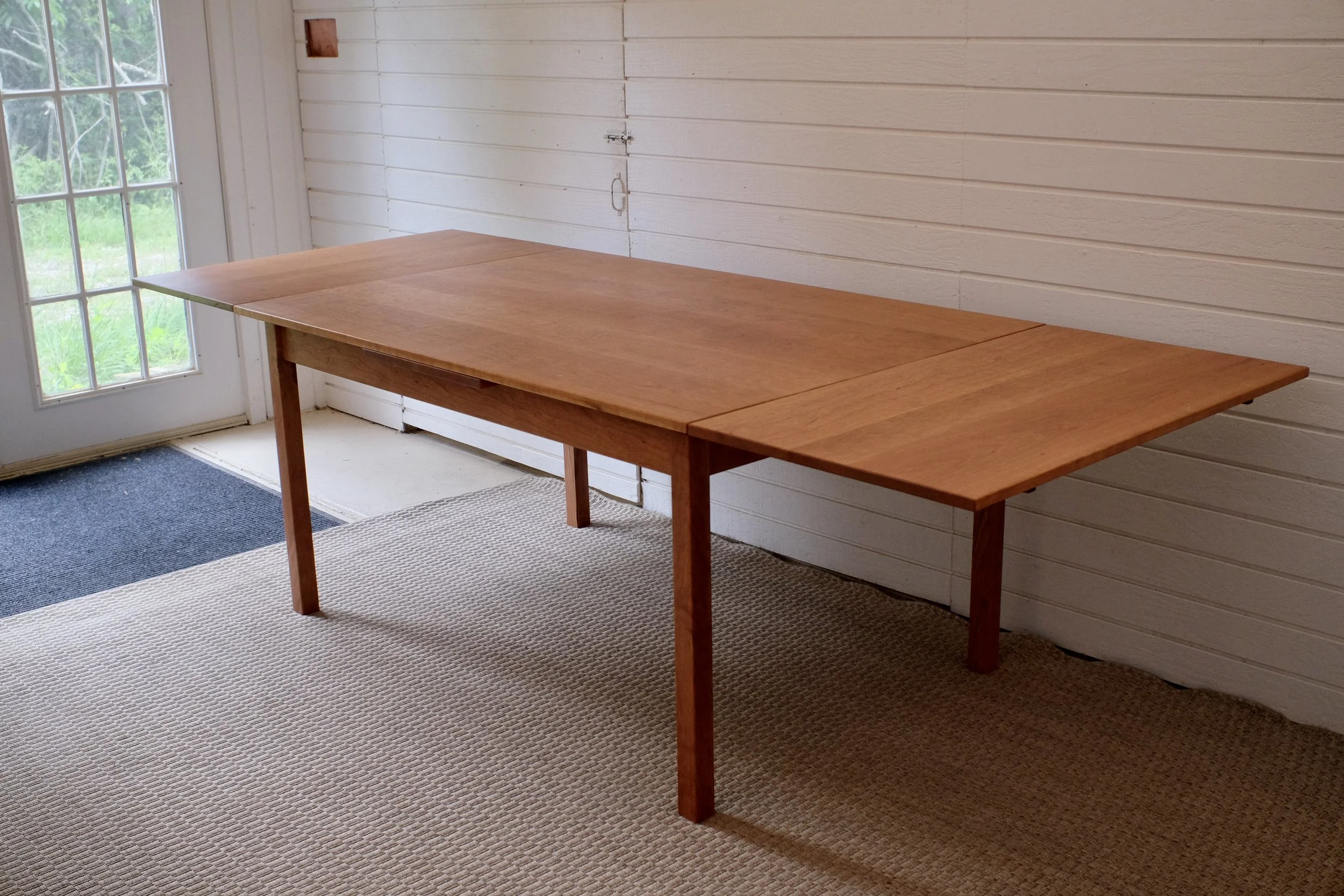 Empty wooden table in a room near a glass door with a view of greenery outside.