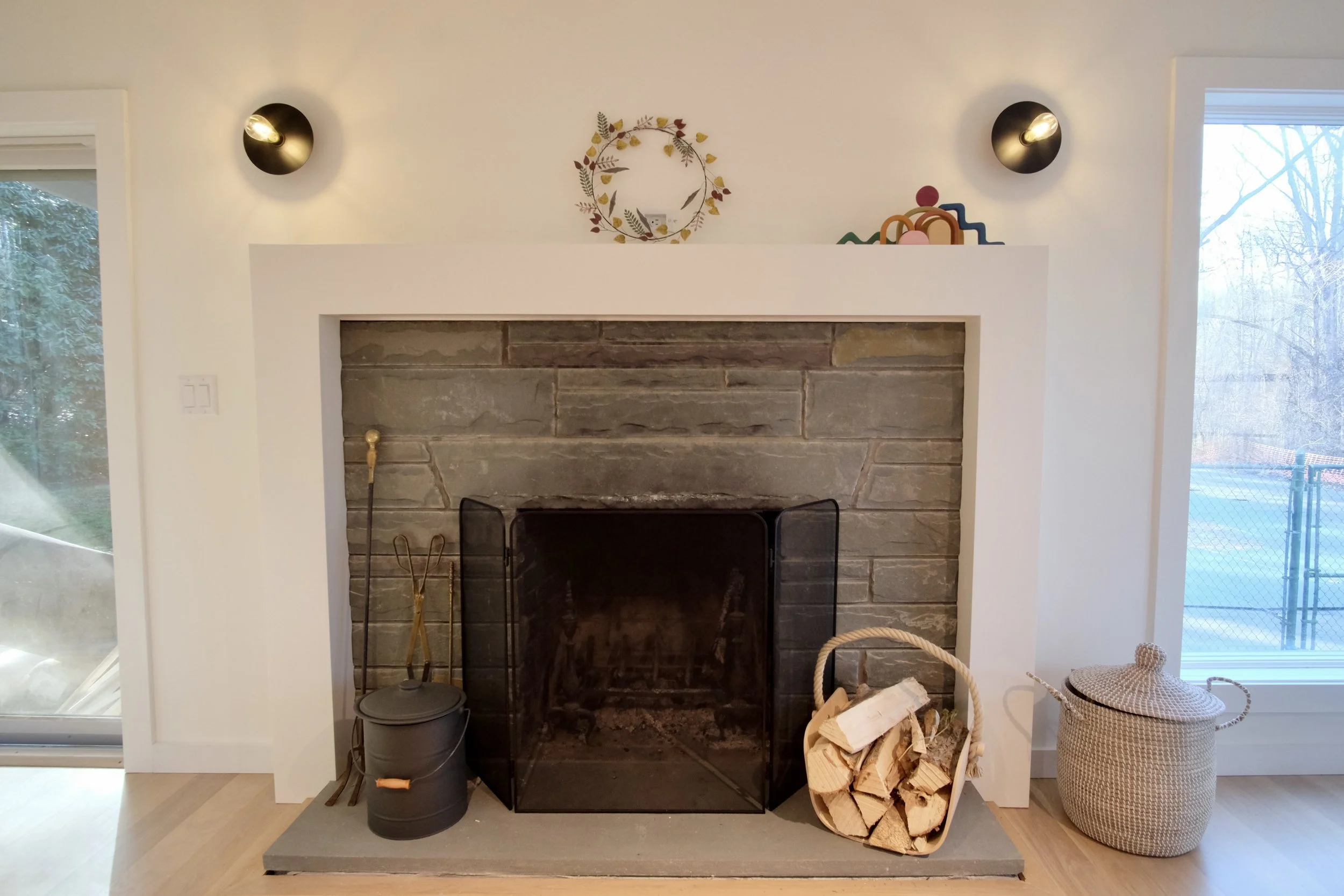 Living room fireplace with firewood, tools, and decor.