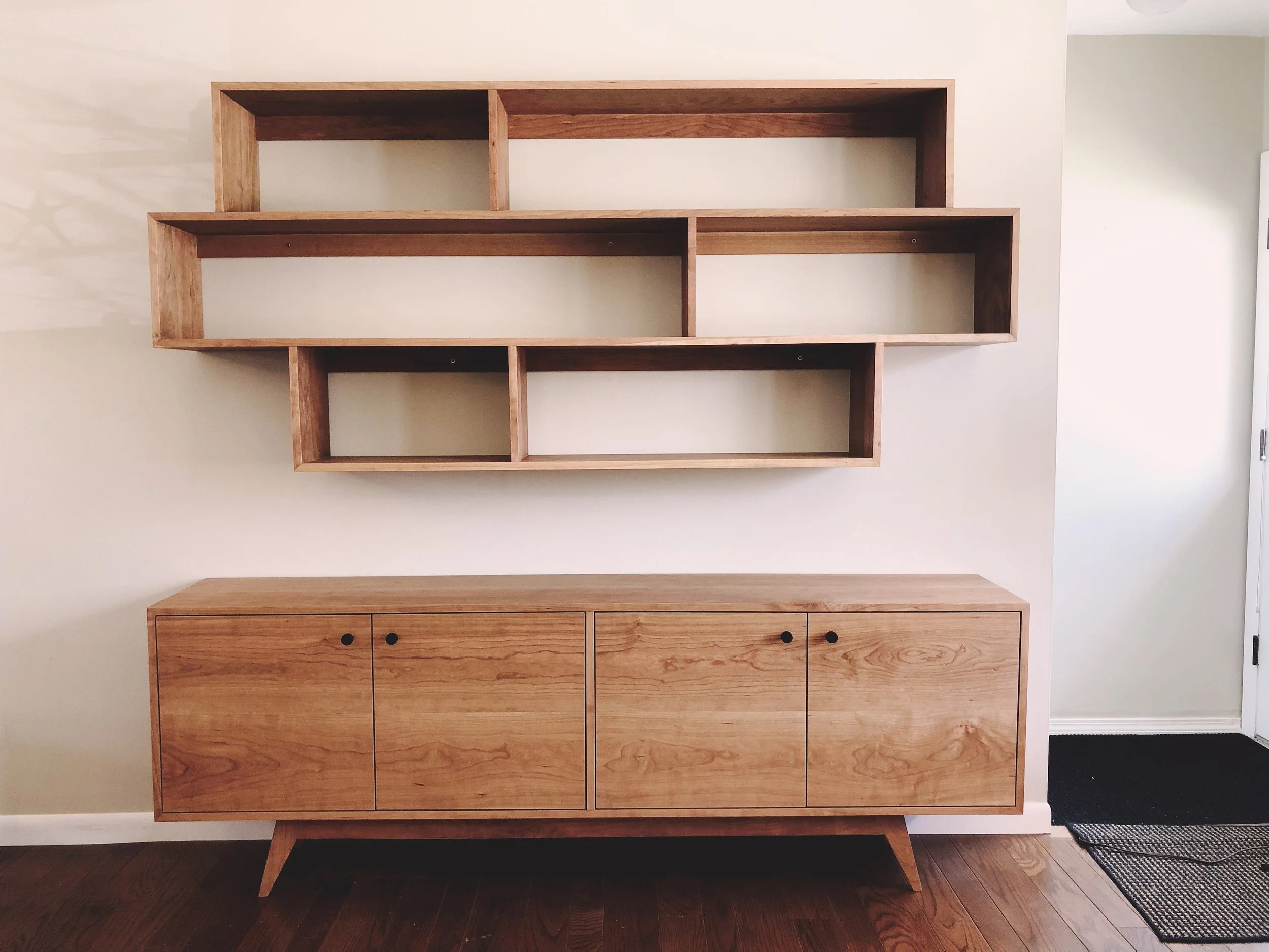 Wooden sideboard with four doors and round black knobs, and matching wall-mounted open shelving units above.