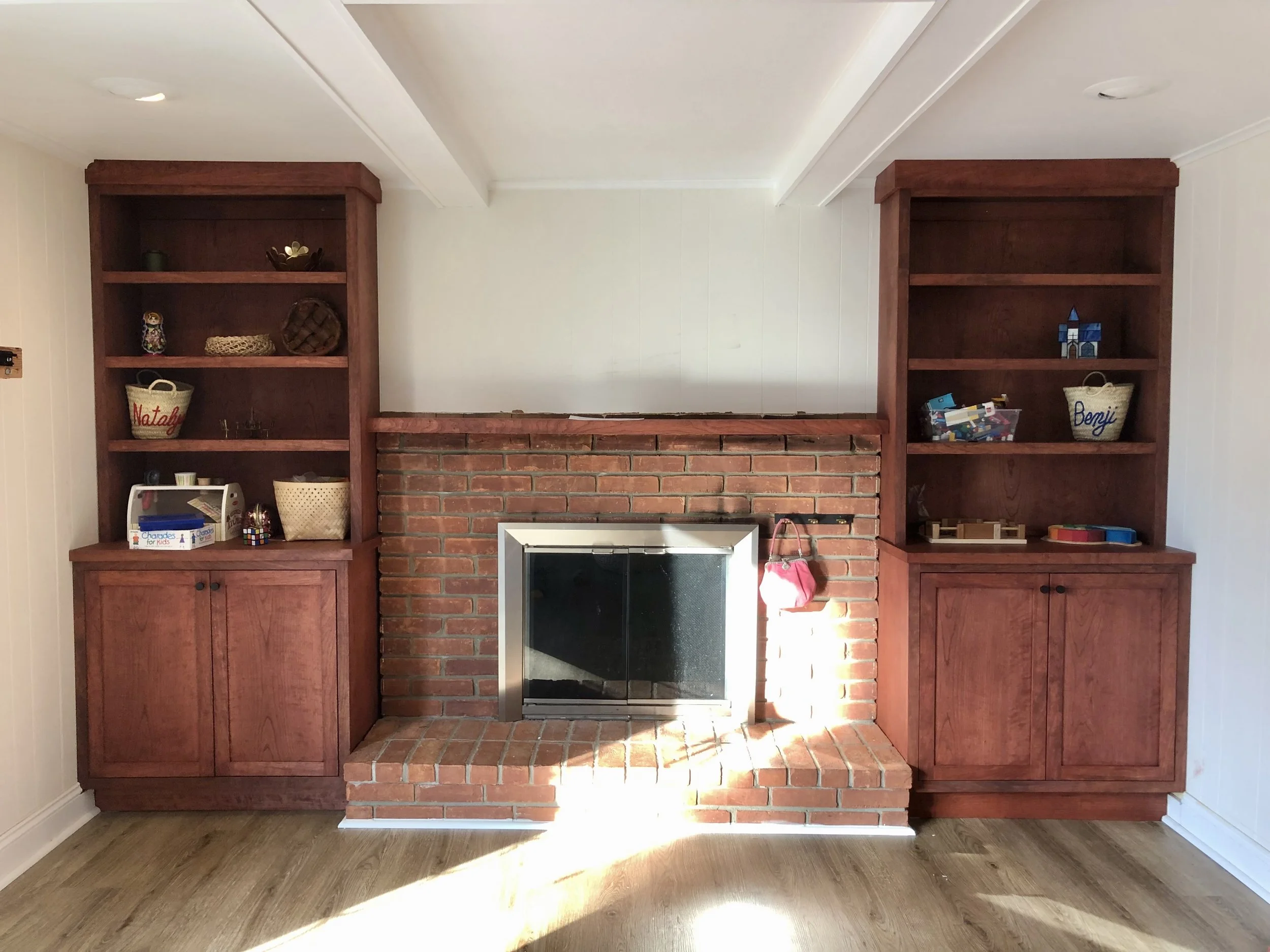 Living room with brick fireplace and two wooden bookshelves filled with decorative items and toys.