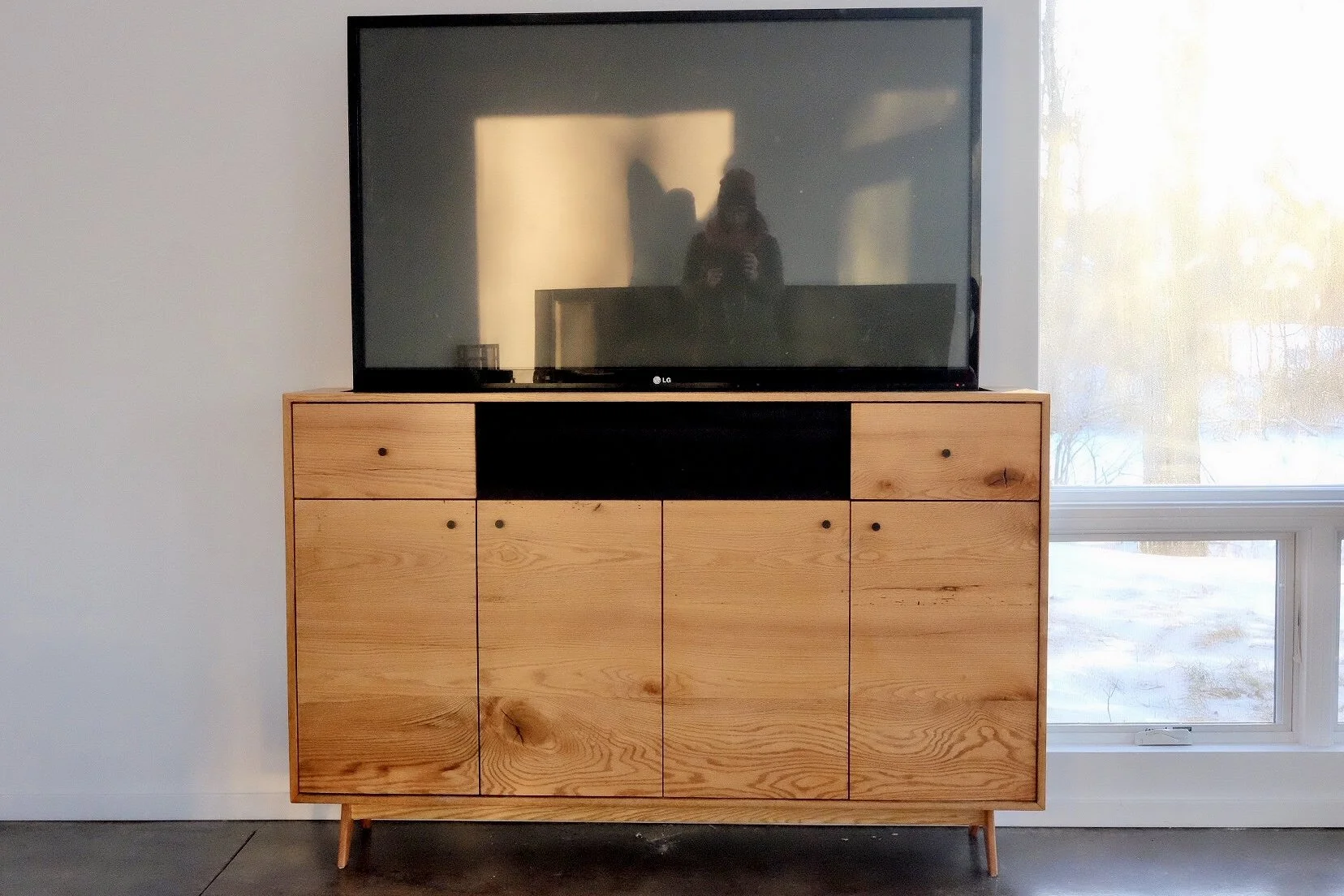 Flat-screen TV on a wooden cabinet near a window with outdoor trees.