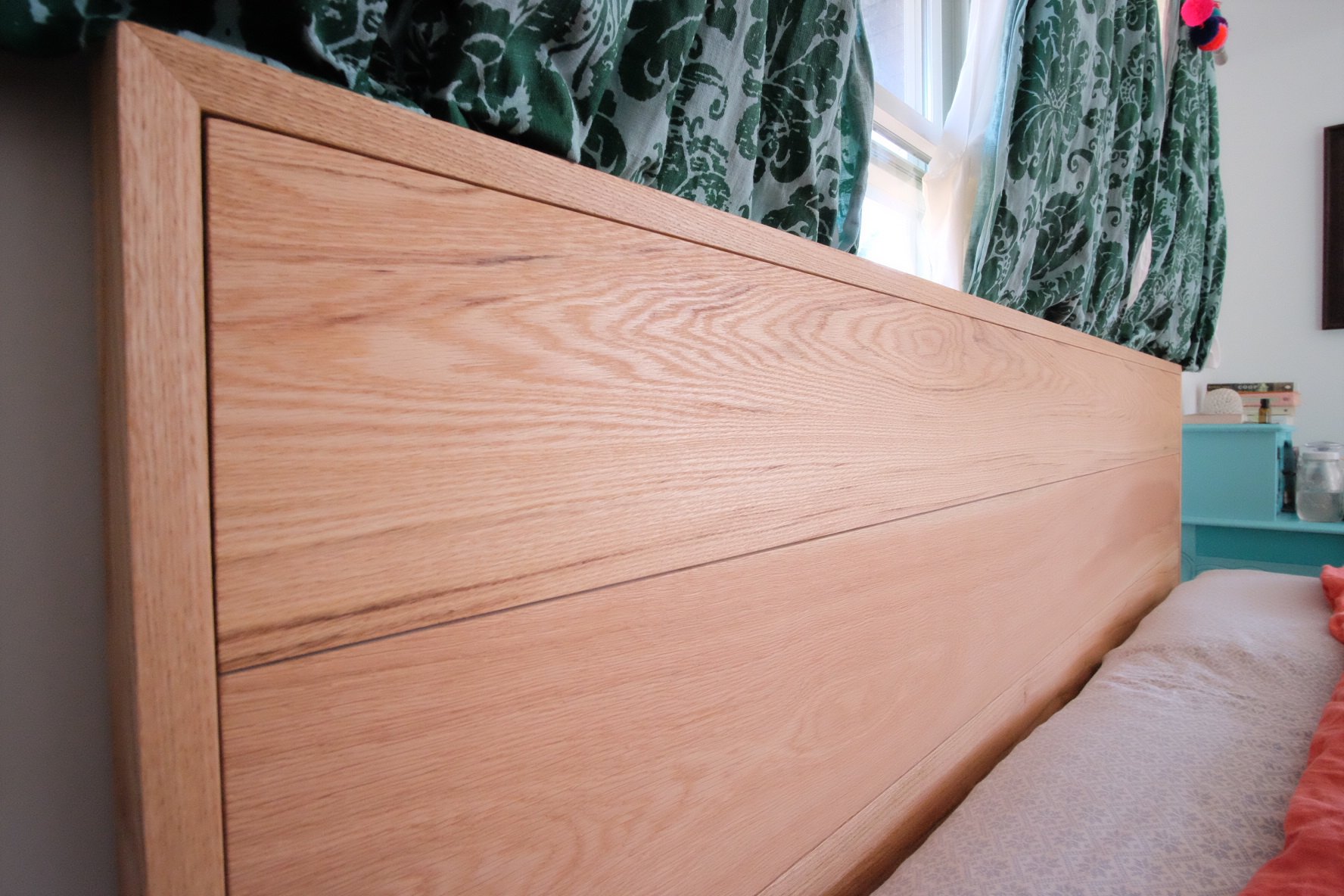 Close-up of a wooden headboard with green curtains and a window in the background.