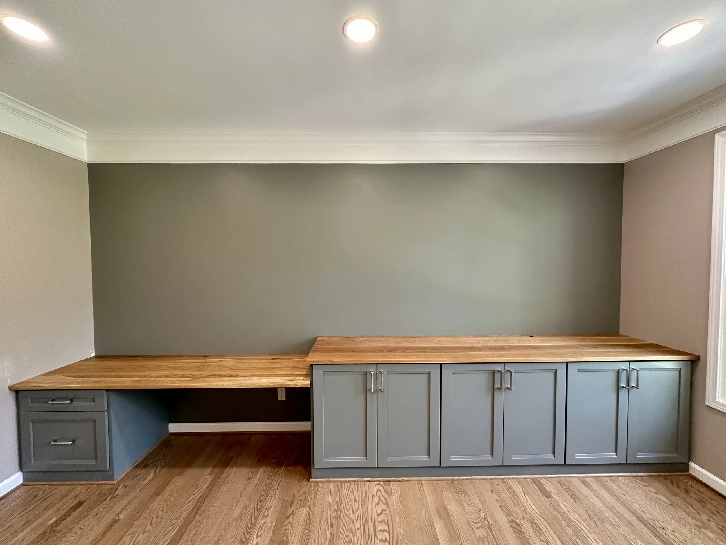 Empty room with unfinished wooden countertop and gray cabinets against a green wall.