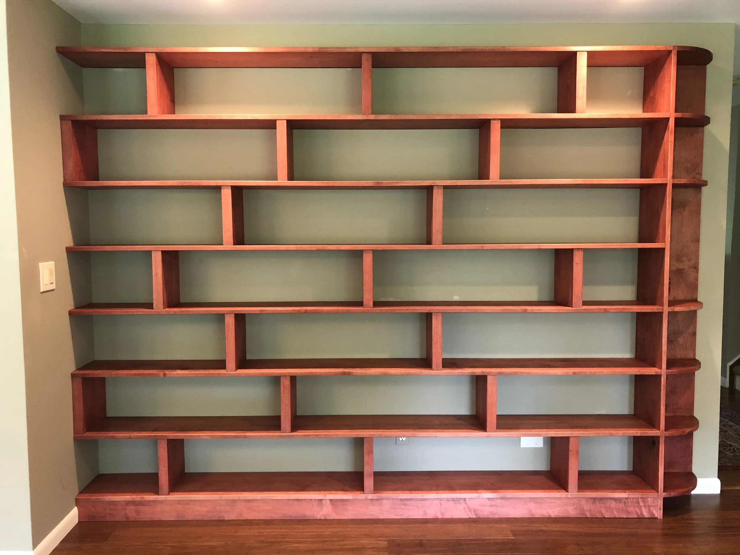 Large wooden bookshelf with multiple compartments against a green wall.