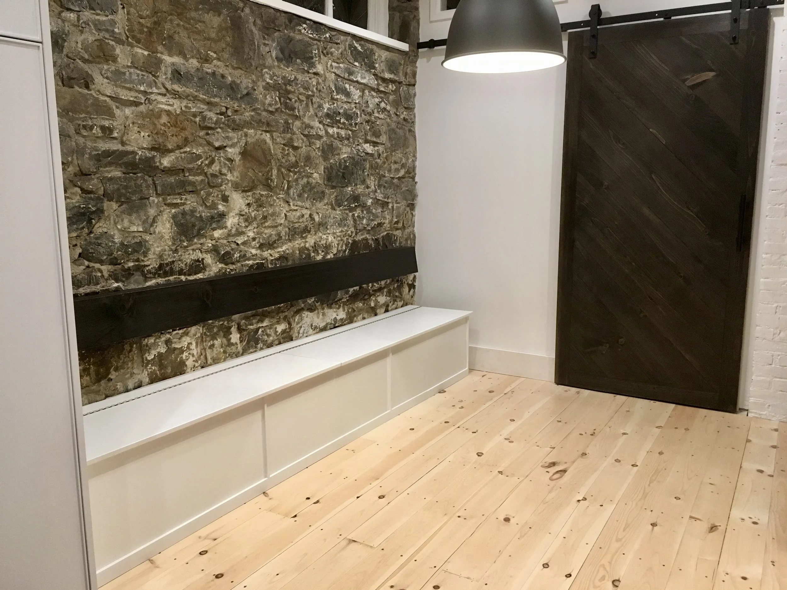 Interior of a room with a stone brick accent wall, wooden floorboards, a black sliding barn door, and a black pendant light hanging from the ceiling.