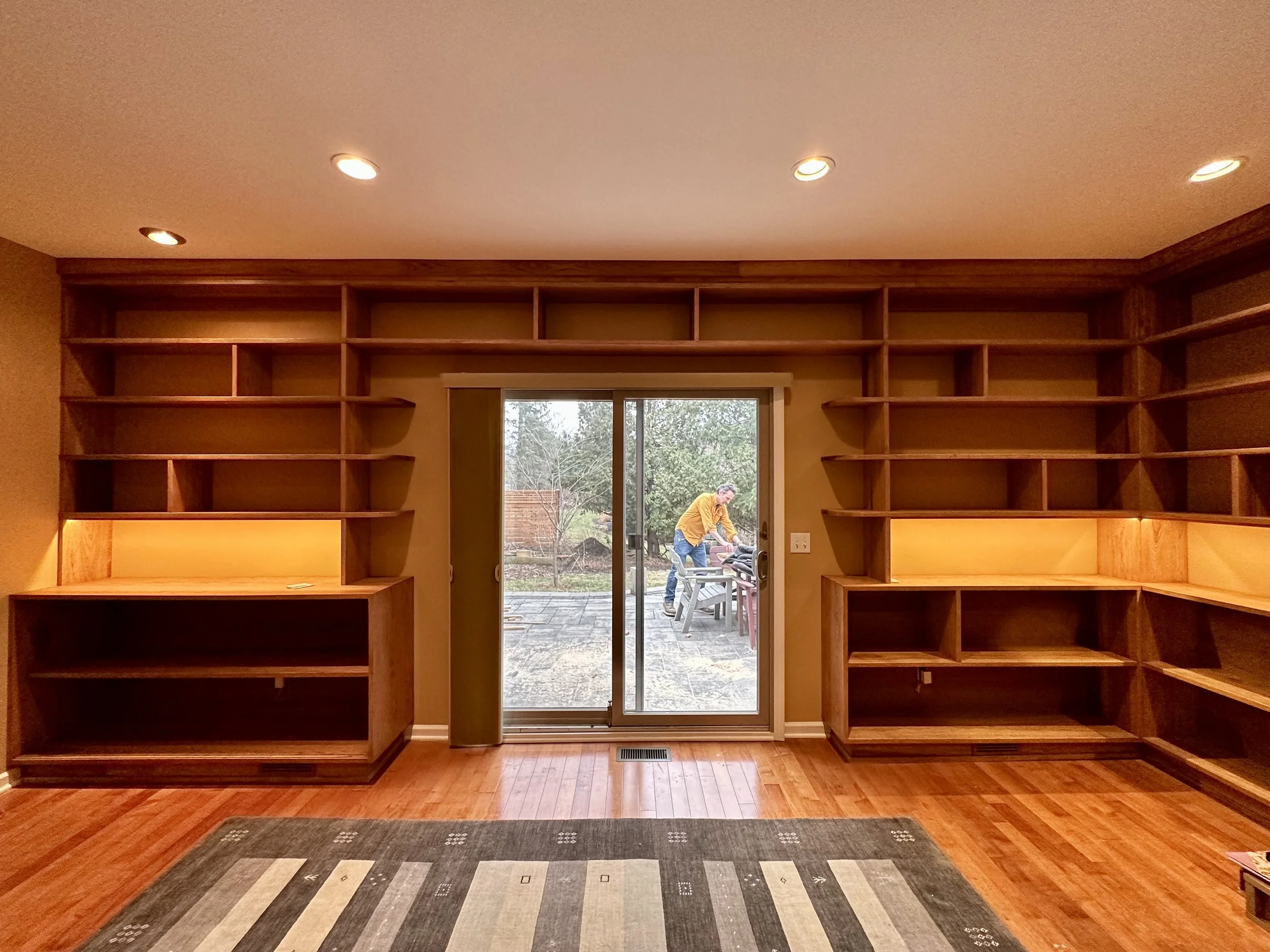 Empty wooden bookshelves on each side of sliding glass doors, with a person outside working at a table.
