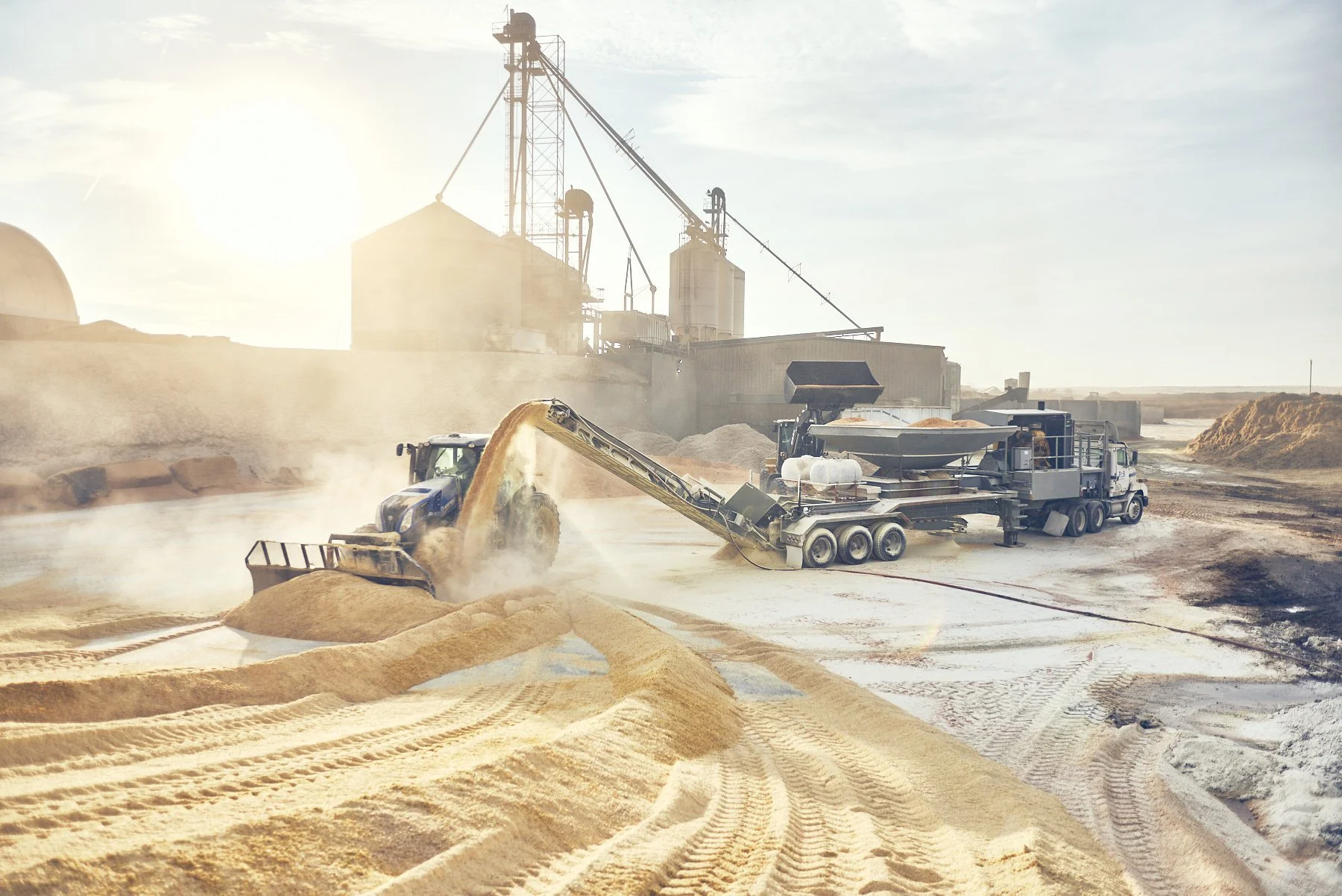 Construction site with machinery including a tractor and conveyor belt, working with sand or gravel during daytime.