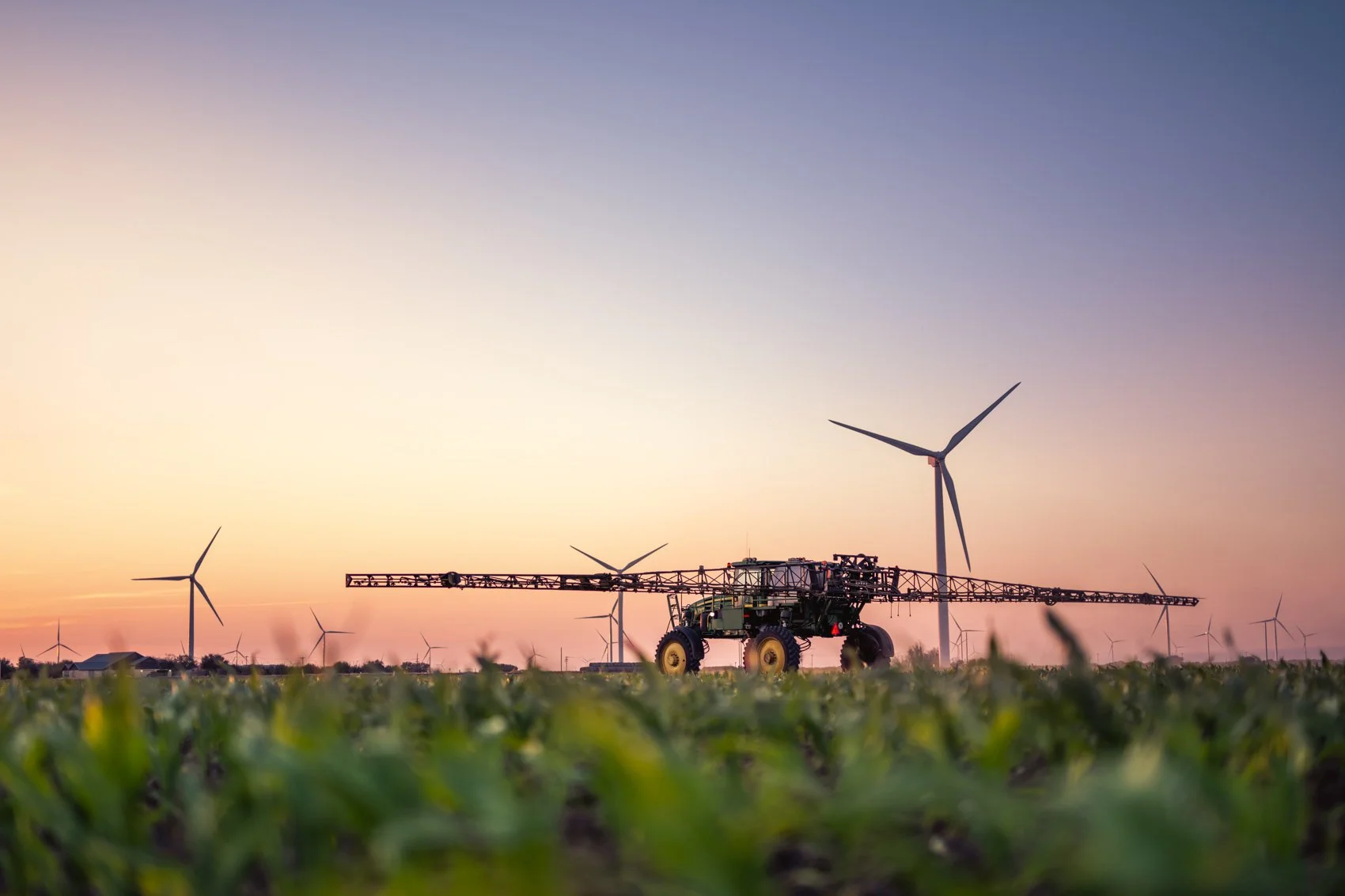 Agricultural field with a tractor and wind turbines at sunset or sunrise.