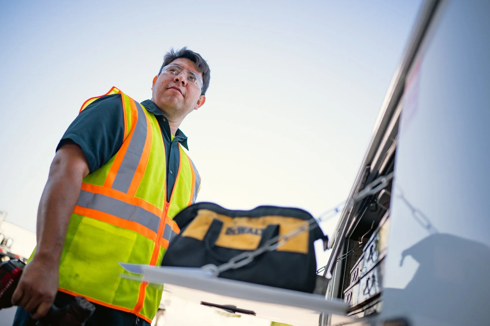 A man wearing safety glasses and a high-visibility vest stands near an emergency vehicle, with a stretcher and medical bag.