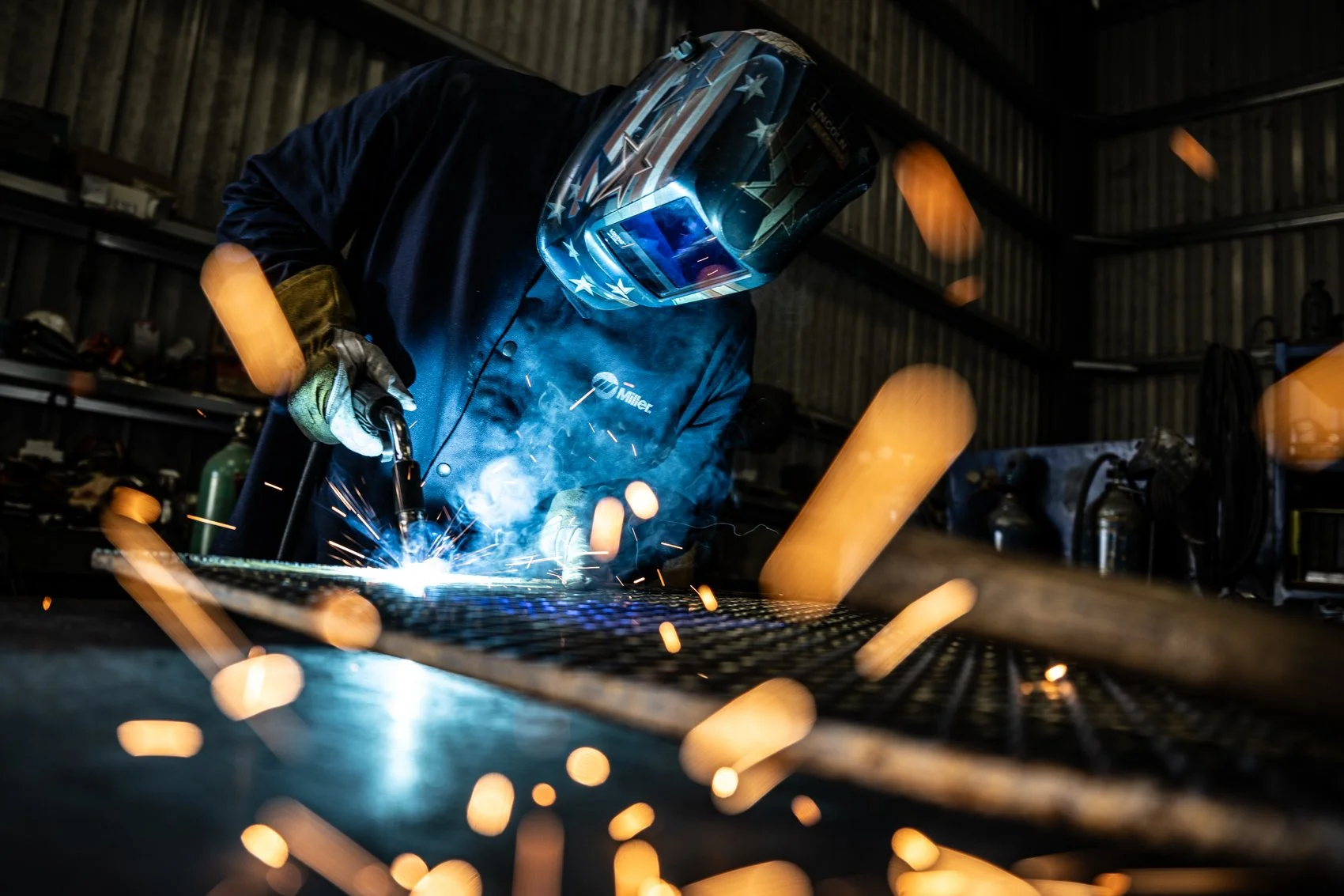 A person welding metal in a workshop, wearing a protective helmet and gloves, with sparks flying around.