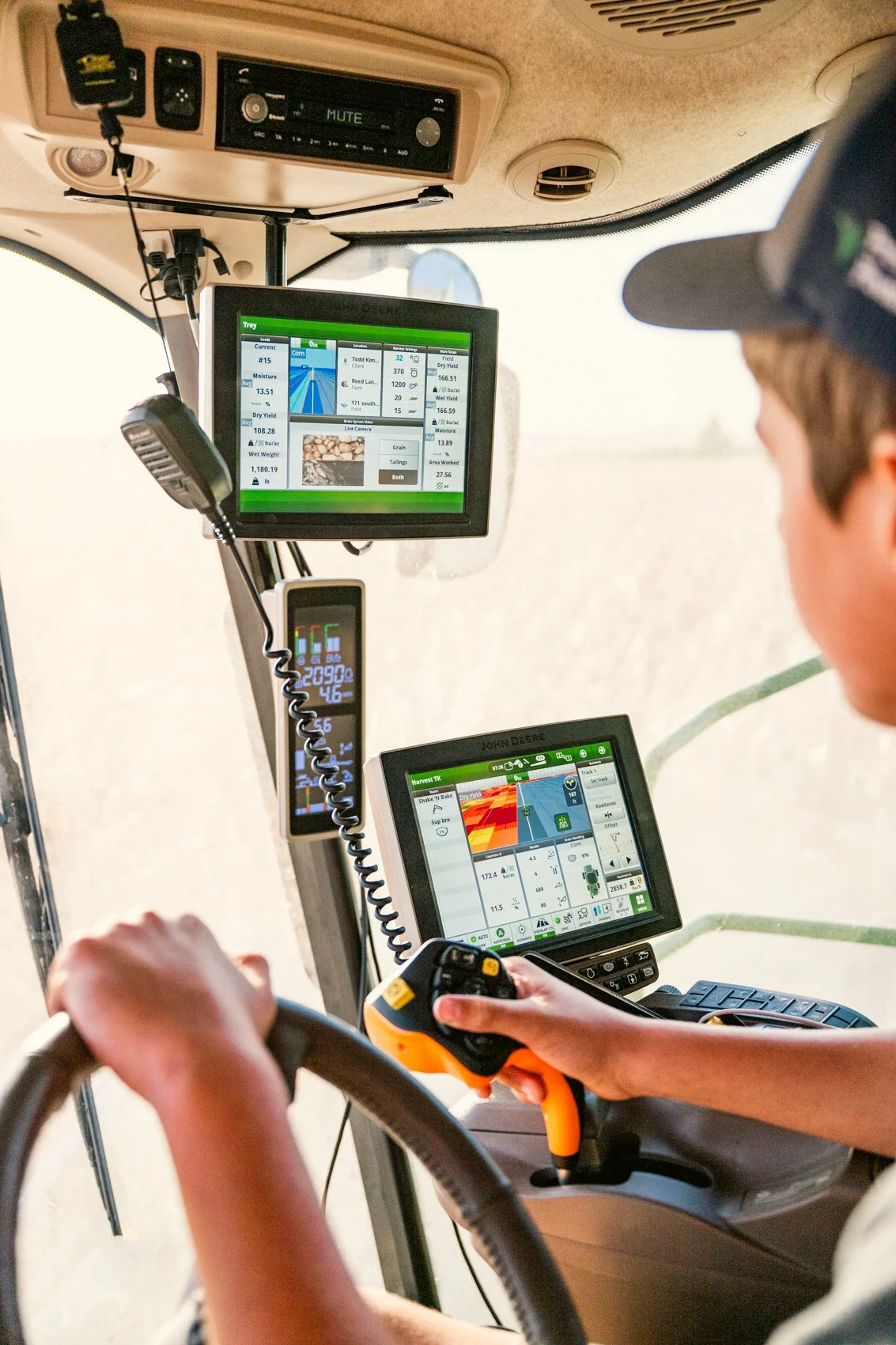 Inside a tractor cab showing a person operating the tractor with various digital displays and controls, including GPS navigation and data screens.