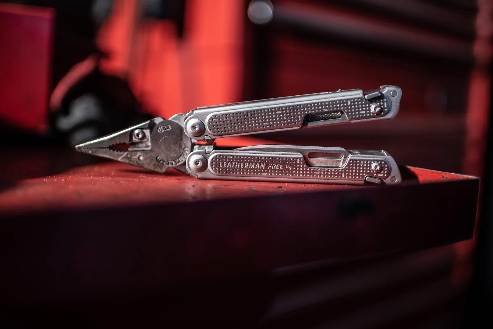 A multitool with pliers and a fold-out blade on a red surface, with a blurred red and black background.