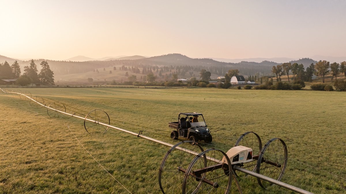 Farmland with spray irrigation system, a utility vehicle, and distant hills and trees at sunset.