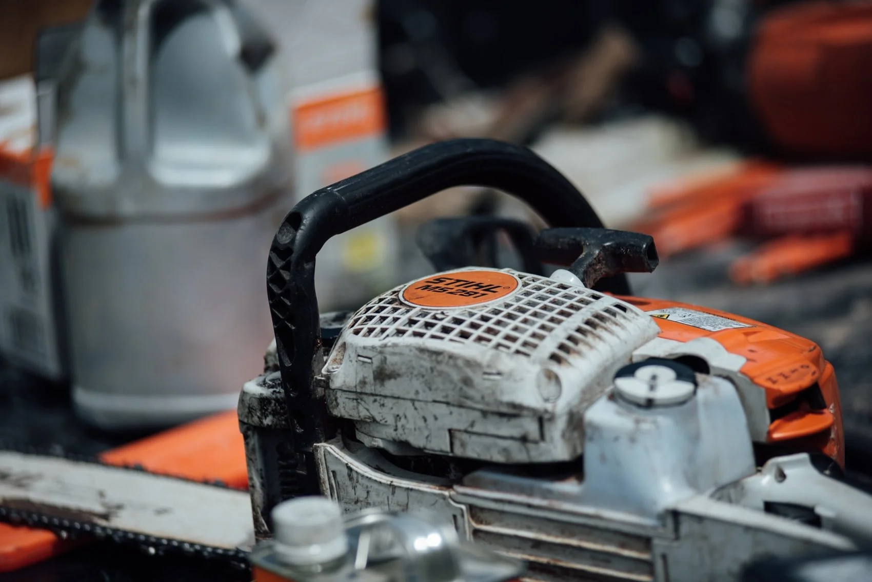 A chainsaw placed on a work surface, with various other tools and containers around it.
