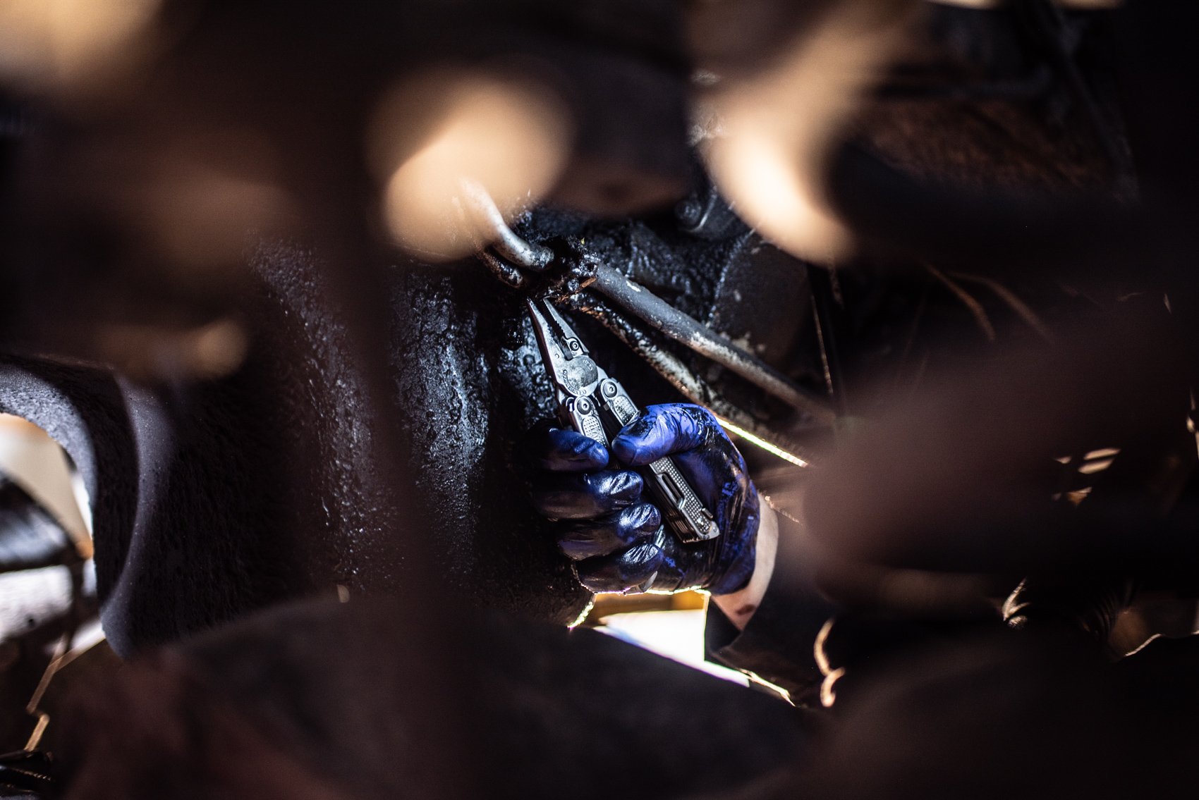 A person wearing blue gloves using a wrench inside a dark, greasy mechanical or automotive engine or machinery compartment.