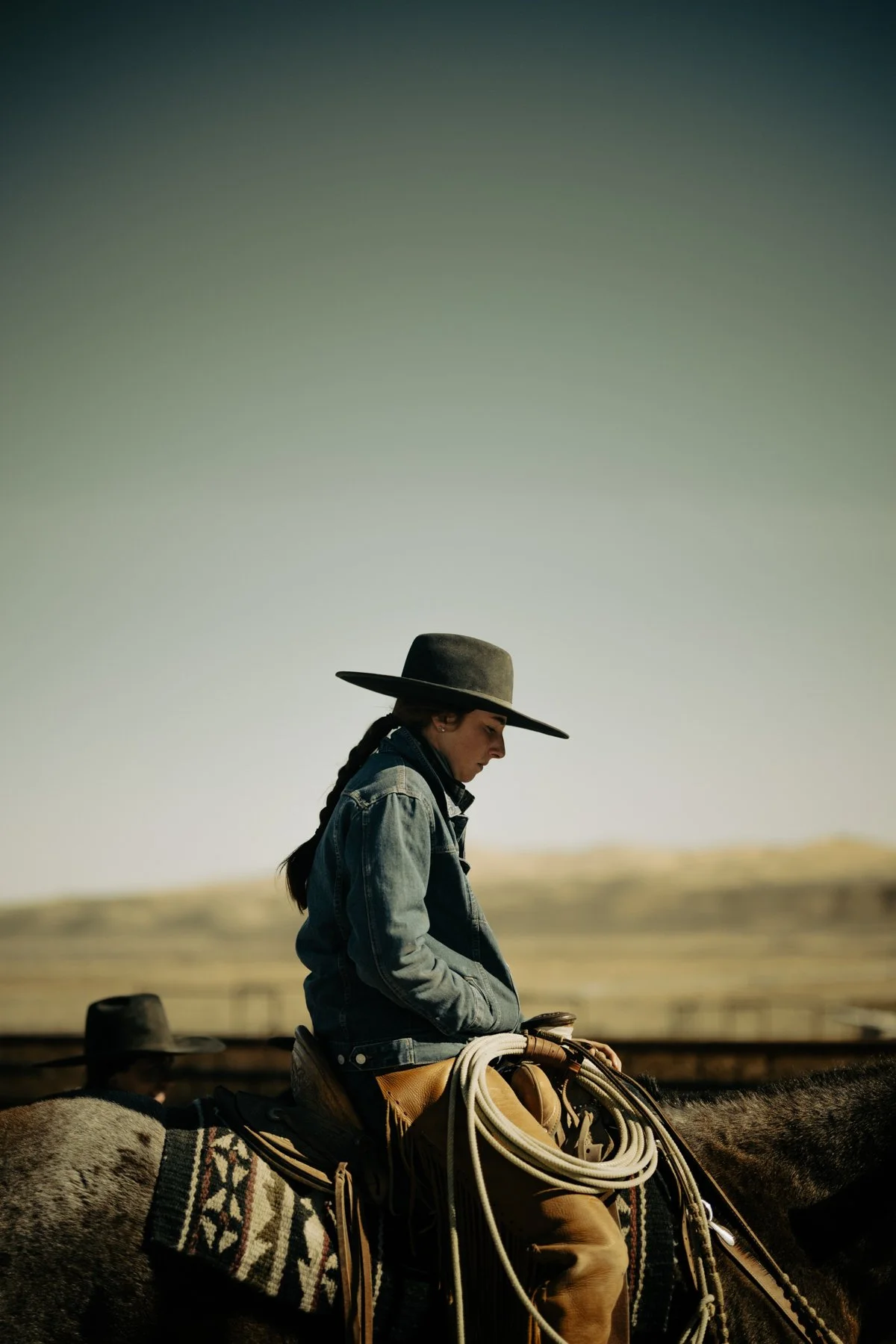 A woman dressed in western attire riding a horse in a desert landscape with clear sky.