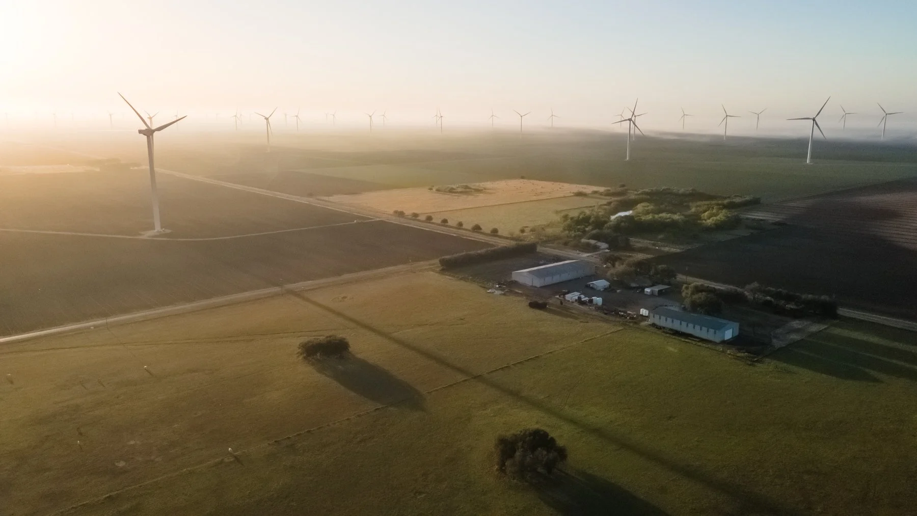 Aerial view of a wind farm with multiple wind turbines across fields at sunset.