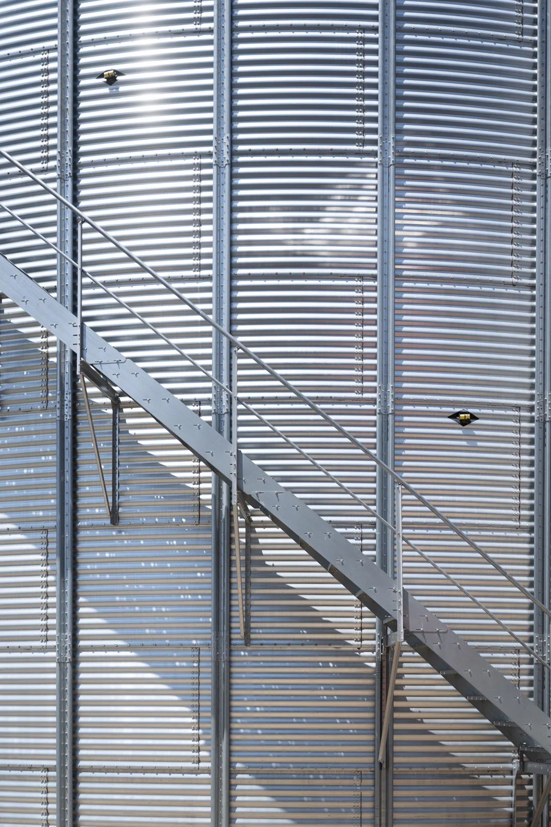 Metal exterior wall of a building with horizontal corrugated panels and an outdoor staircase made of metal with a railing.