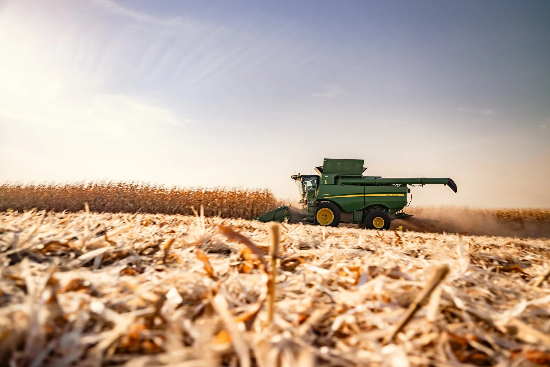 A green combine harvester working in a field during daytime, harvesting crops with a clear sky overhead.