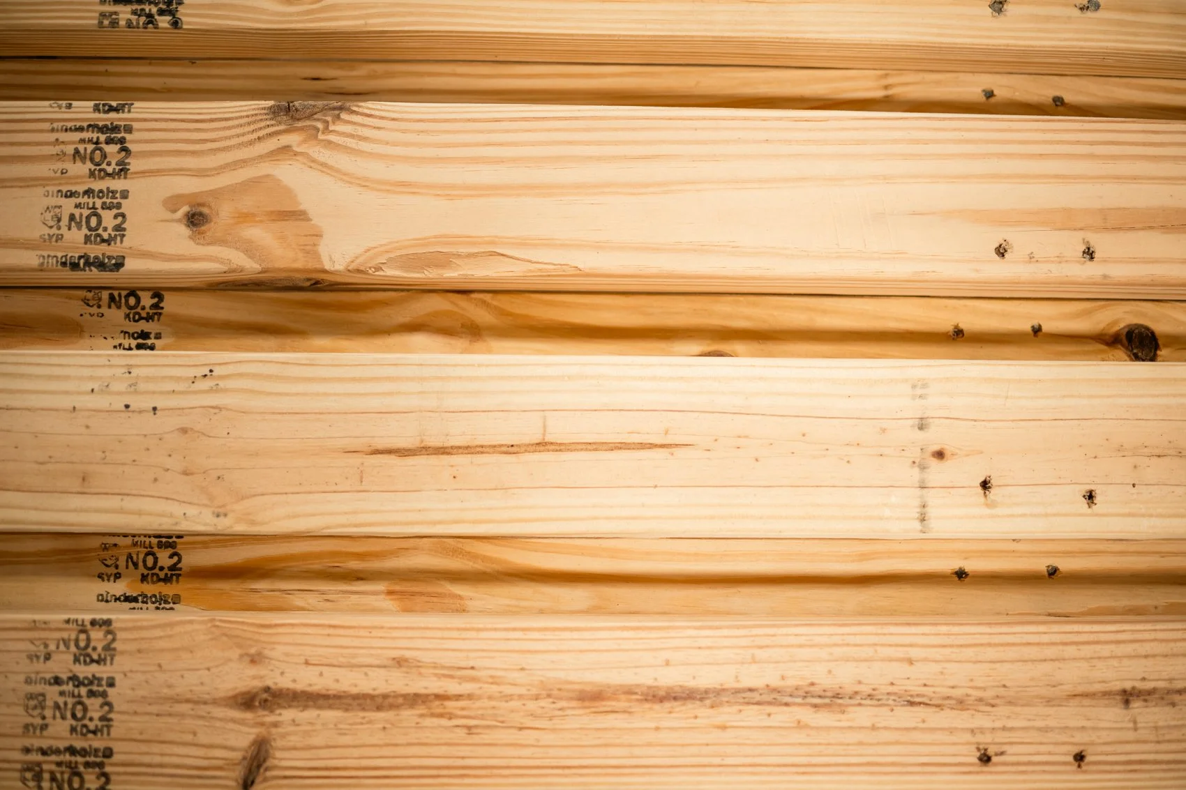 Close-up of several horizontal light-colored wooden planks with visible grain patterns, knots, and some stamped markings on the left side.
