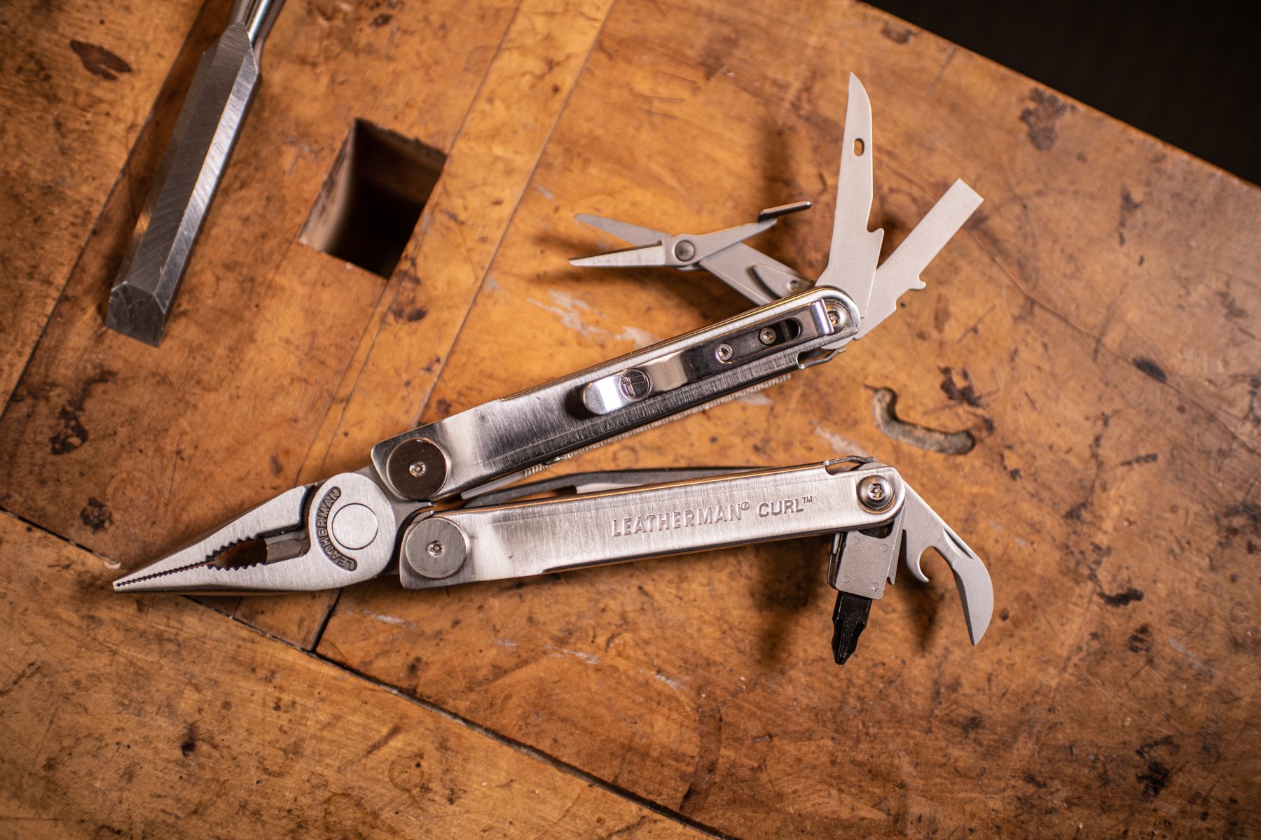 Multi-tool pliers with various tools extended, resting on a wooden workbench.