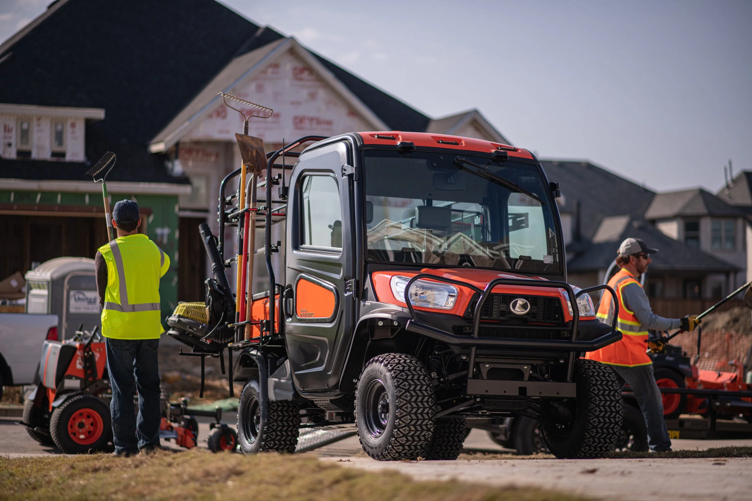 Construction workers operating a utility vehicle on a residential street, with houses under construction in the background.