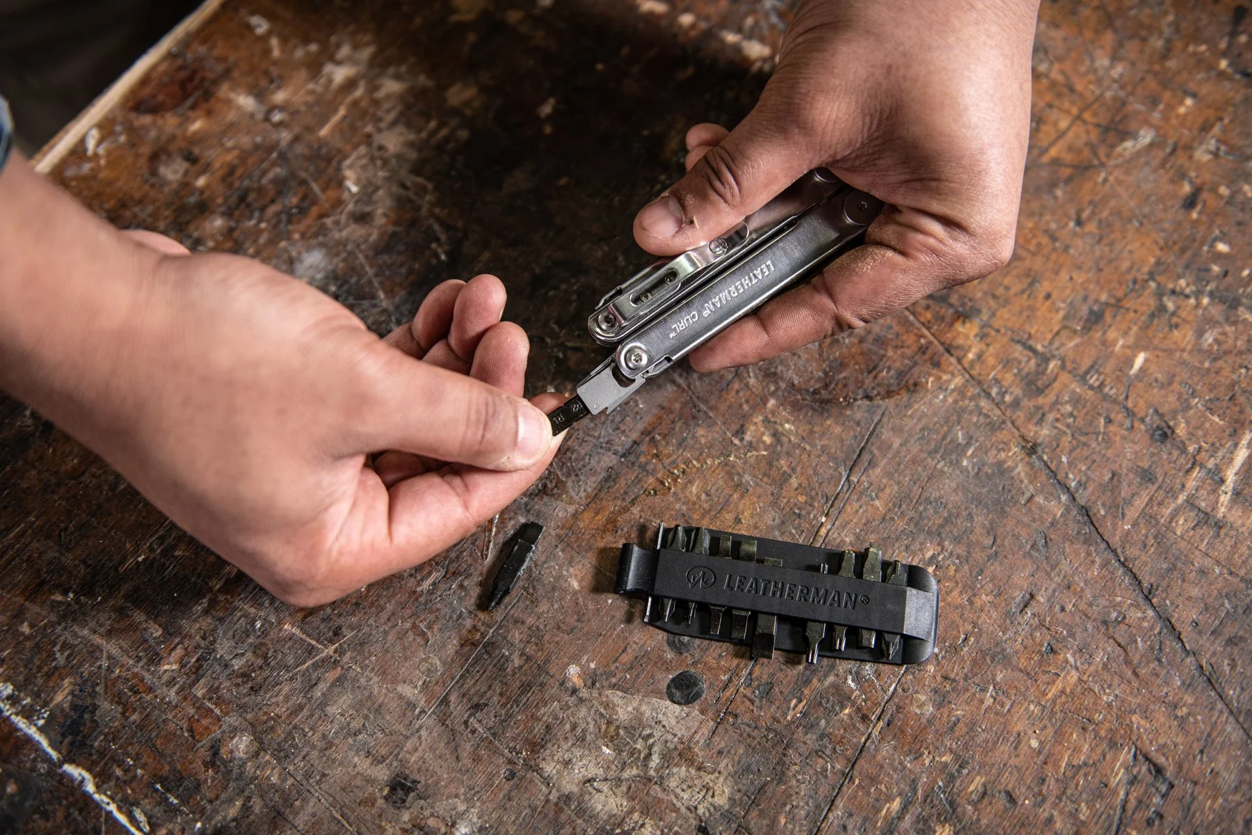 Hands working with a leather craft multitool and a set of interchangeable blades on a wooden workbench.