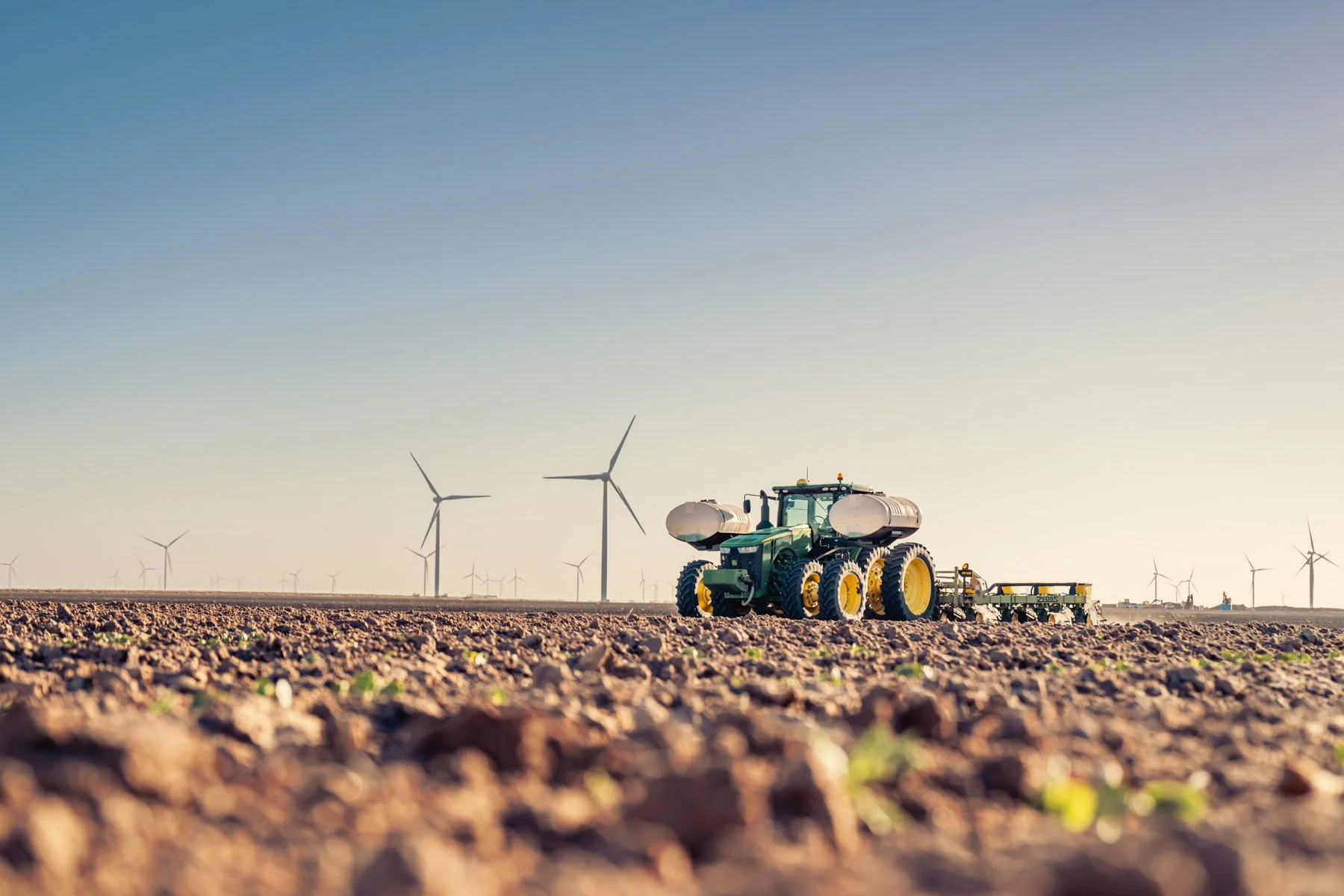 A tractor working in a field with multiple wind turbines in the background under a clear sky.