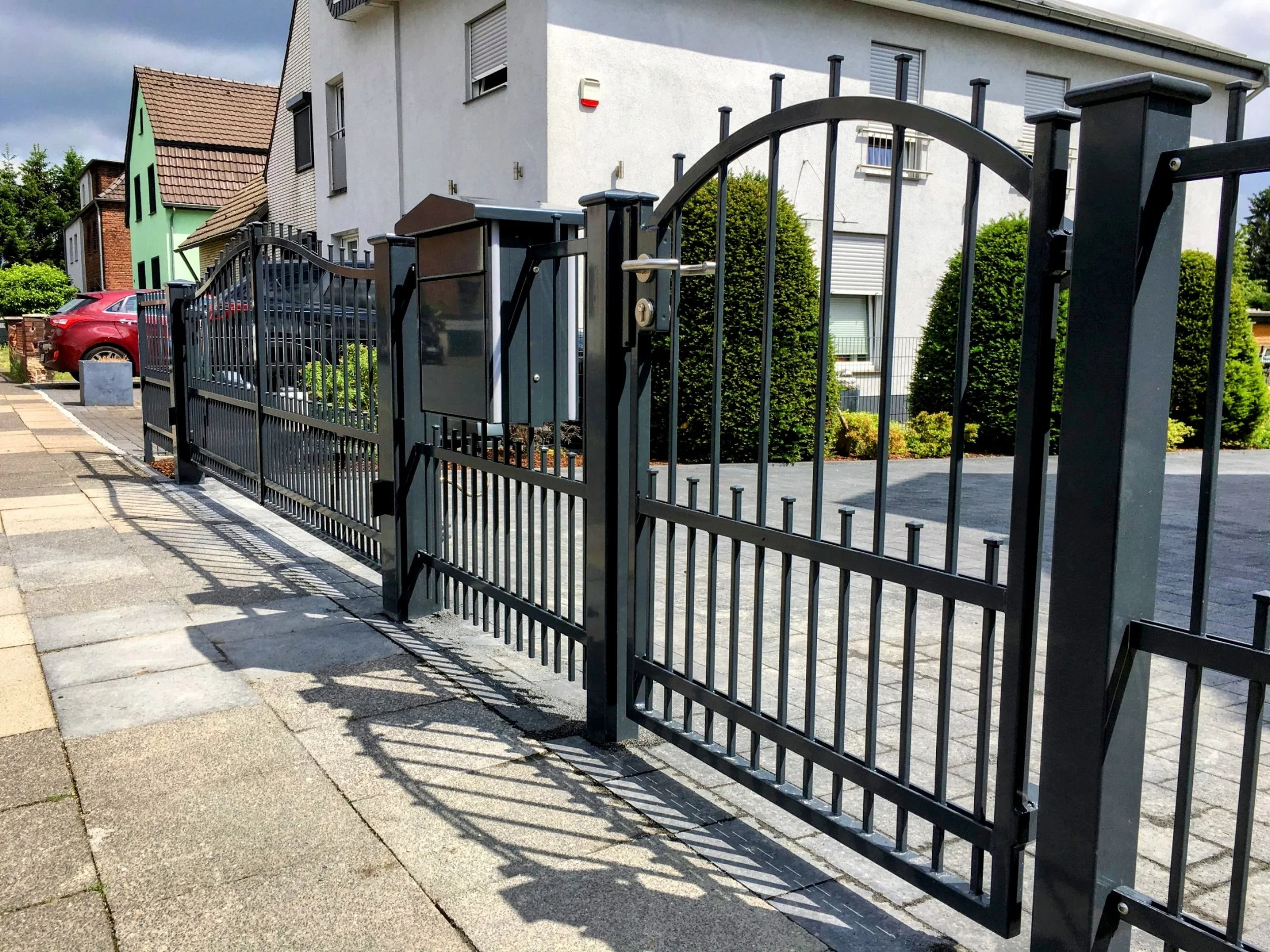 Schmiedeeiserne Gartentür mit Zaun und einer modernen Wohnanlage im Hintergrund.