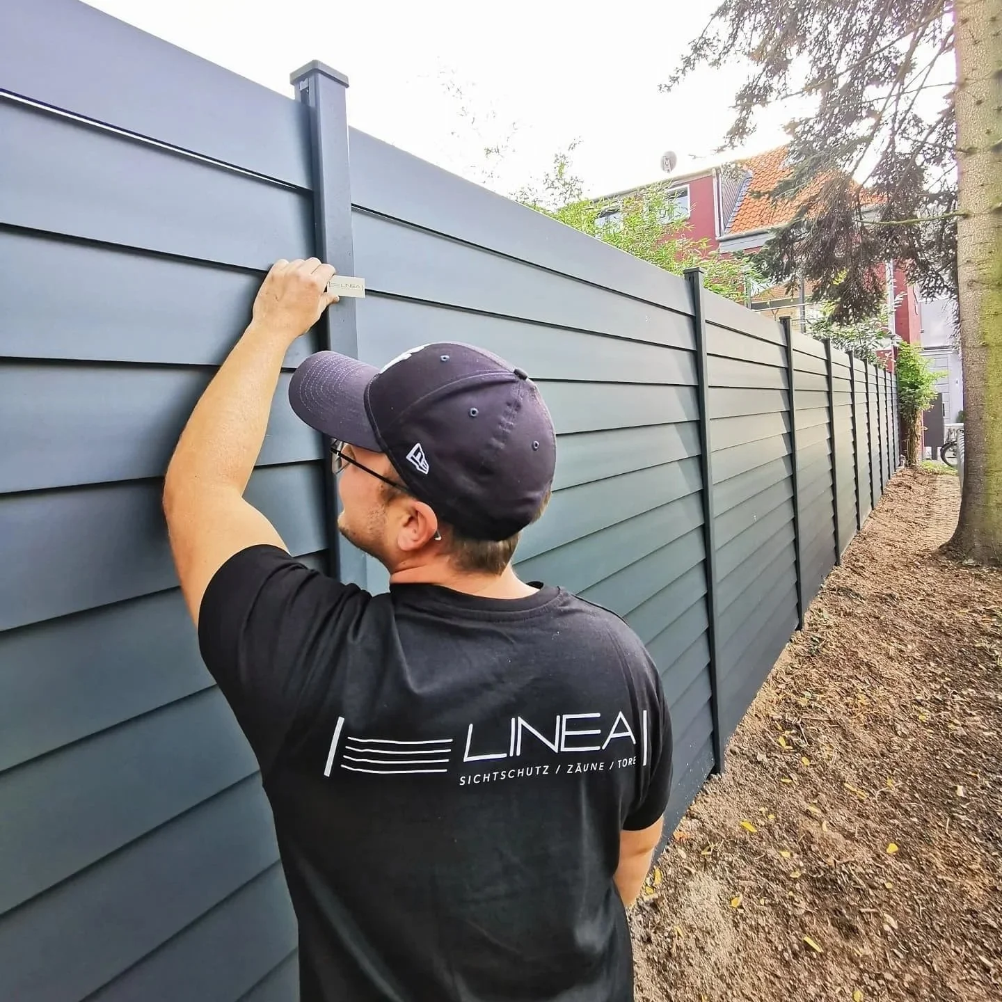 Mann befestigt eine Garten- oder Zaunlatte an einem dunklen Metallzaun mit einer Wasserwaage.