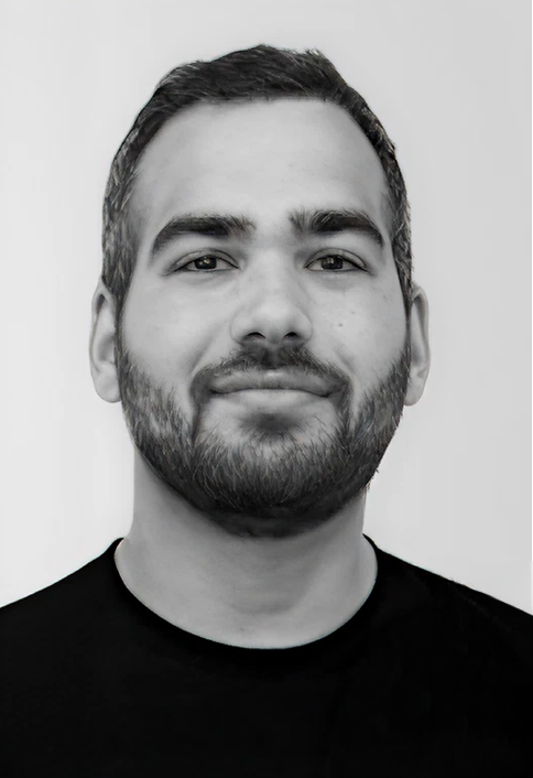 Black and white portrait of a young man with short dark hair, a beard, and a slight smile, wearing a black shirt.