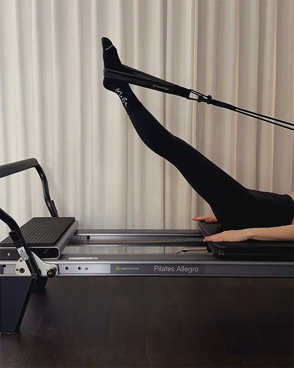 Person performing Pilates exercise on a Pilates Allegro reformer with a resistance band around their foot Lower and Lift, Feet in straps