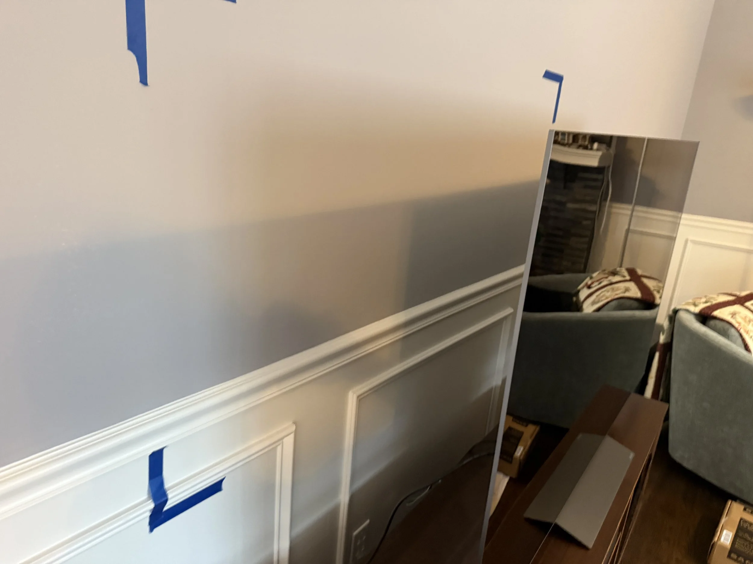 A living room with a wall mirror, couches with patterned pillows, and a wooden shelf with a laptop and boxes.