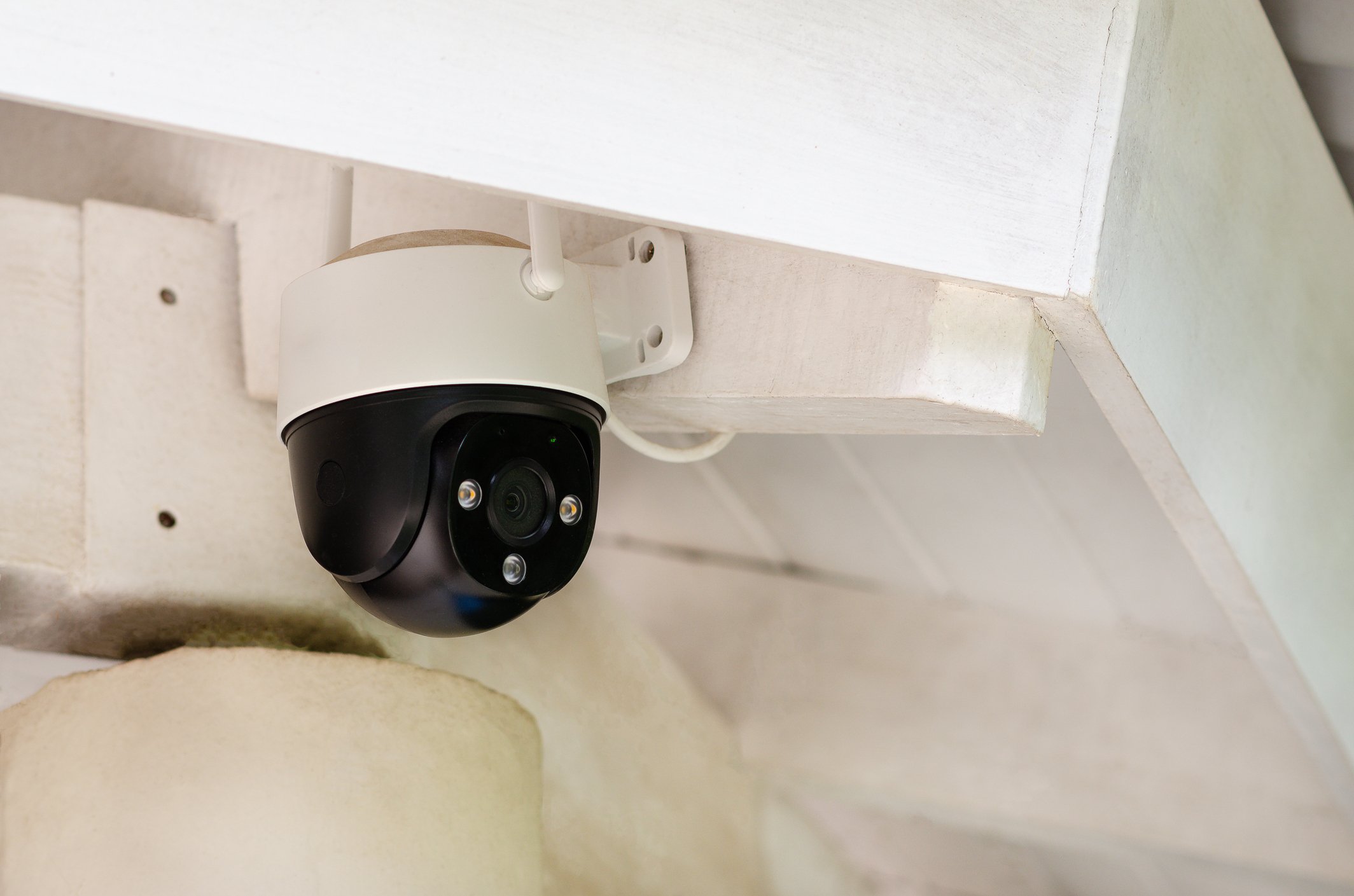 Security camera mounted under a white wooden shelf.